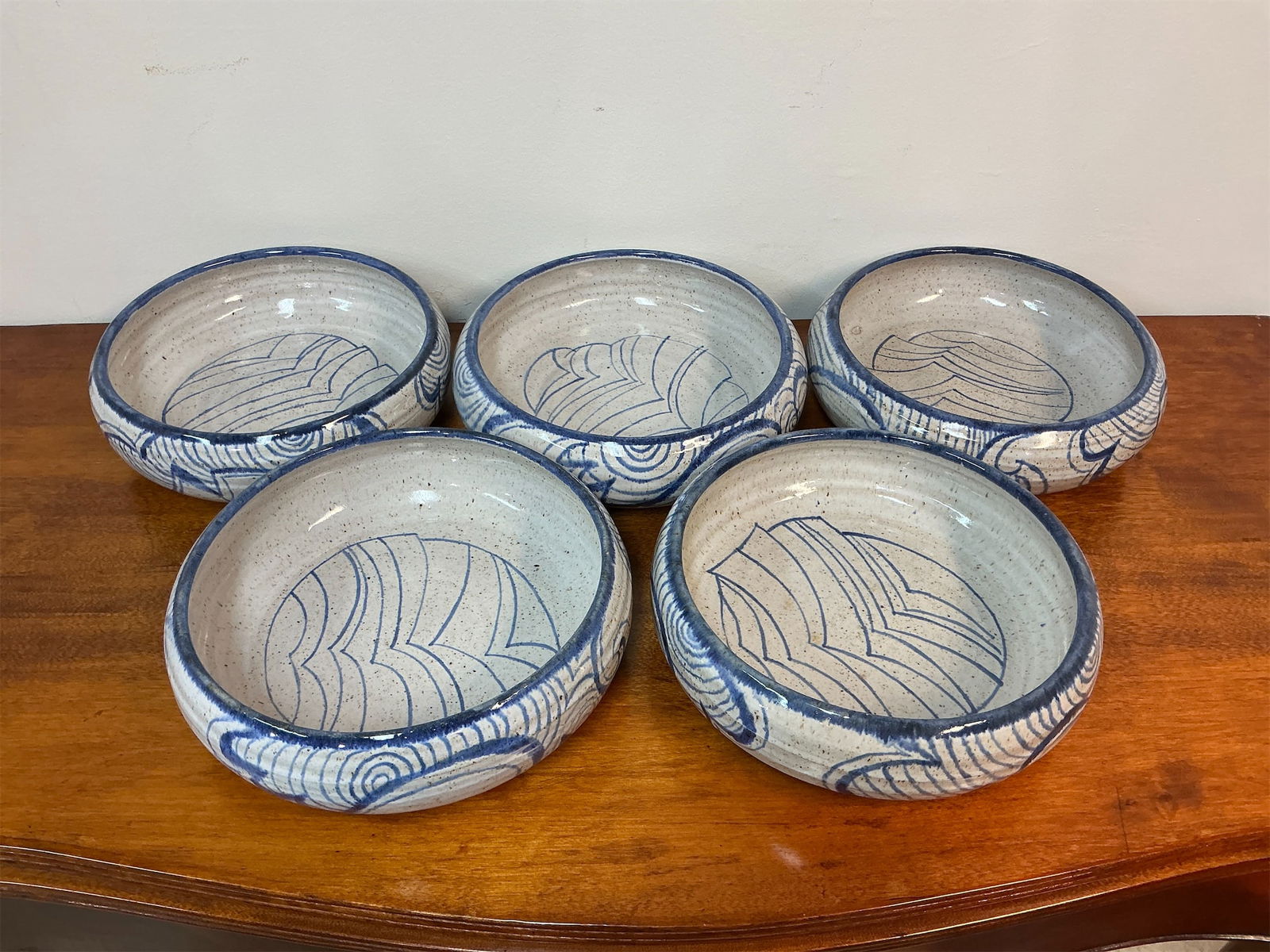 Adrien Studio Stoneware Pottery Bowls - Set of 7: Set of seven studio stoneware pottery bowls, signed by the talented artist Adrien, showcases a unique blend of craftsmanship and artistry. Each bowl features a captivating design with intricate blue