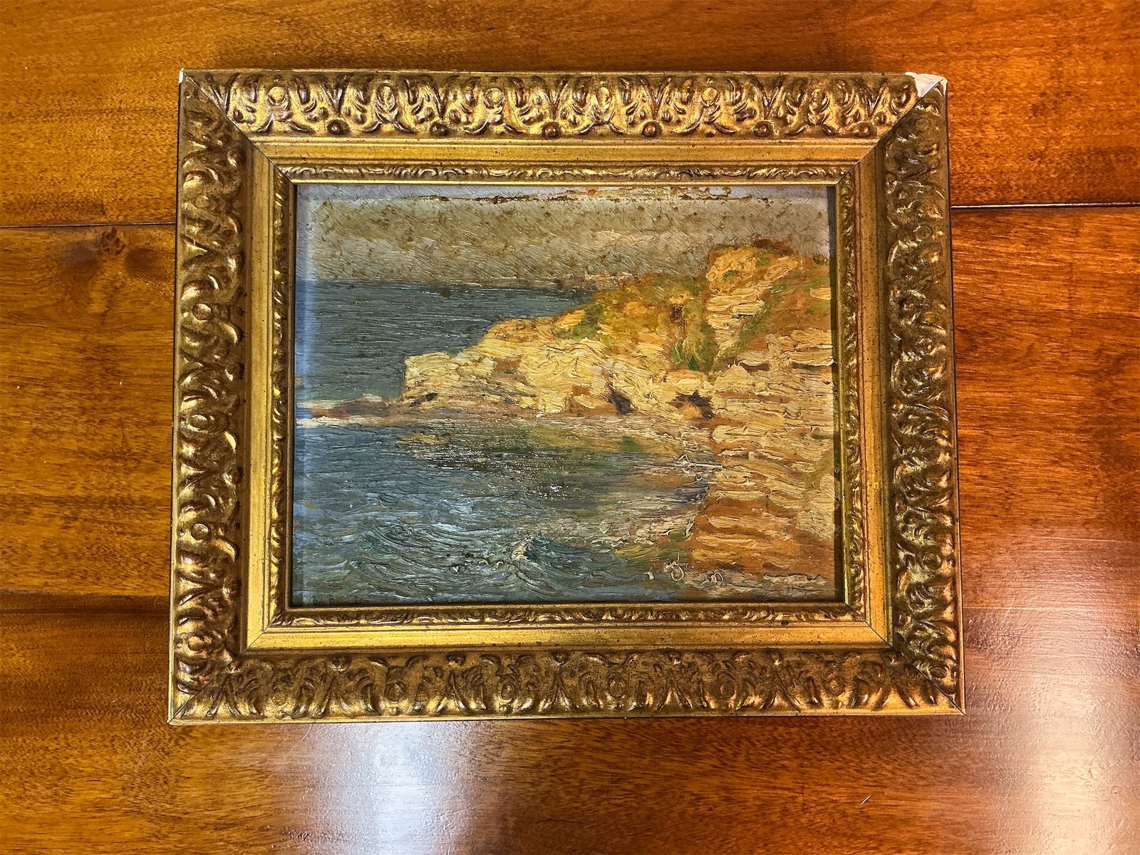 Antique oil on canvas of seascape: This exquisite antique oil on canvas seascape captures a serene coastal scene with its rich textures and vibrant colors. The painting features striking rocky cliffs meeting gentle waves, reflecting
