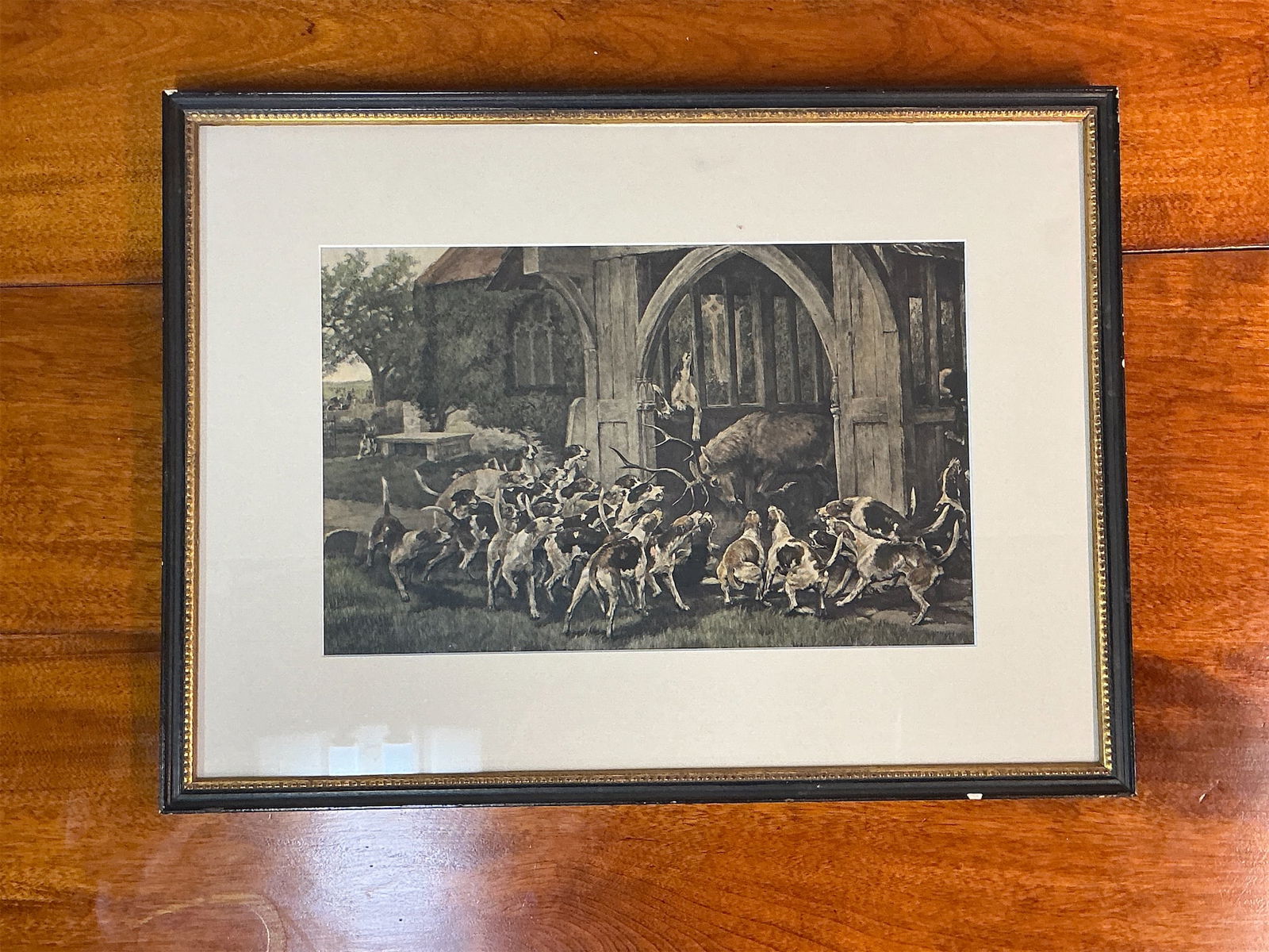 Antique colored engraving of Hounds and a Stag: Antique colored engraving depicting a dynamic scene of hounds pursuing a stag. The artwork features a lively group of hounds gathered around the entrance of a rustic setting, with the stag