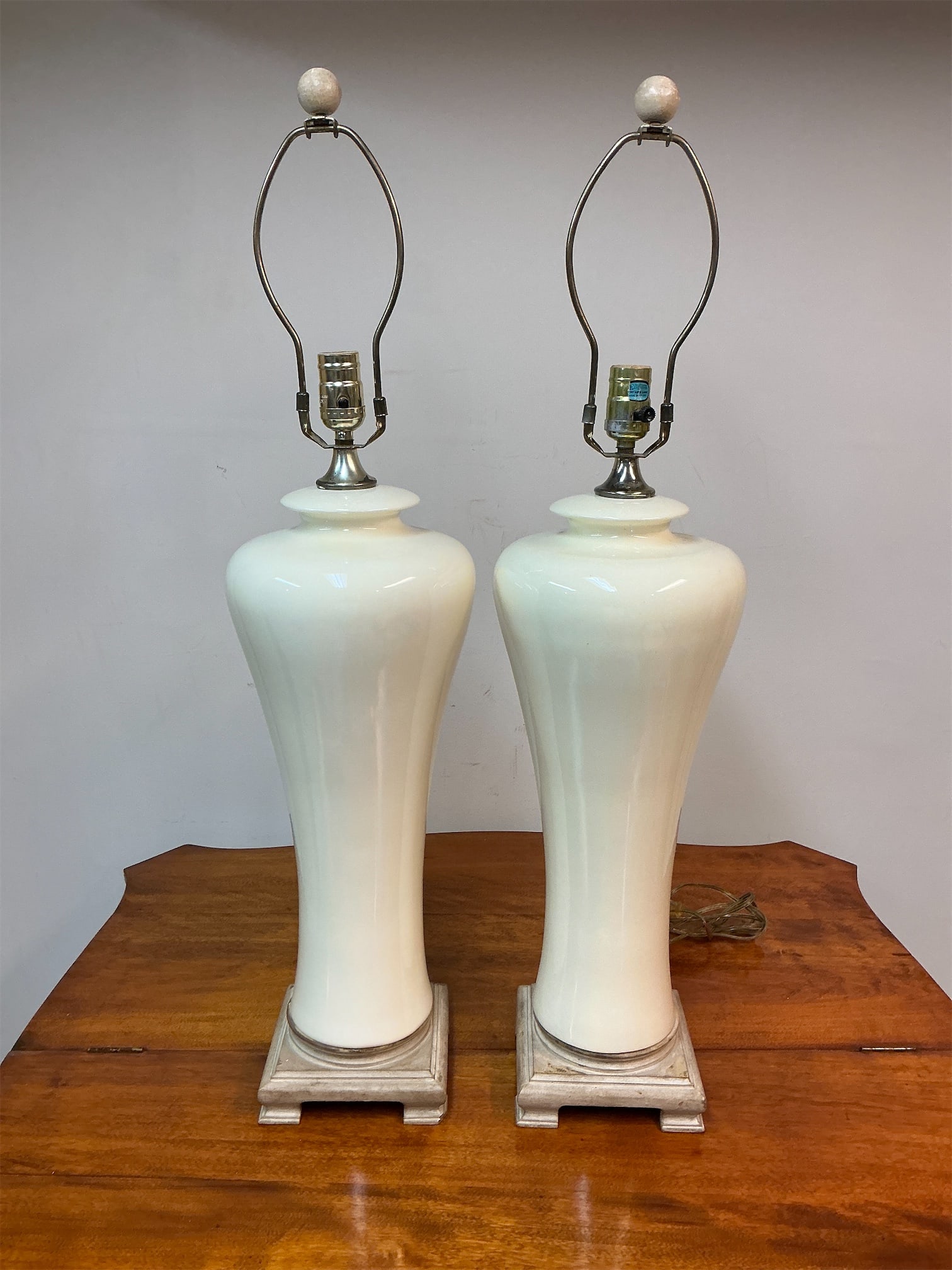 Pair of Off-white ceramic lamps: Pair of off-white ceramic lamps features a gracefully elongated design, perfect for adding a touch of sophistication to any space. Each lamp stands proudly on a sturdy square base with a complementary