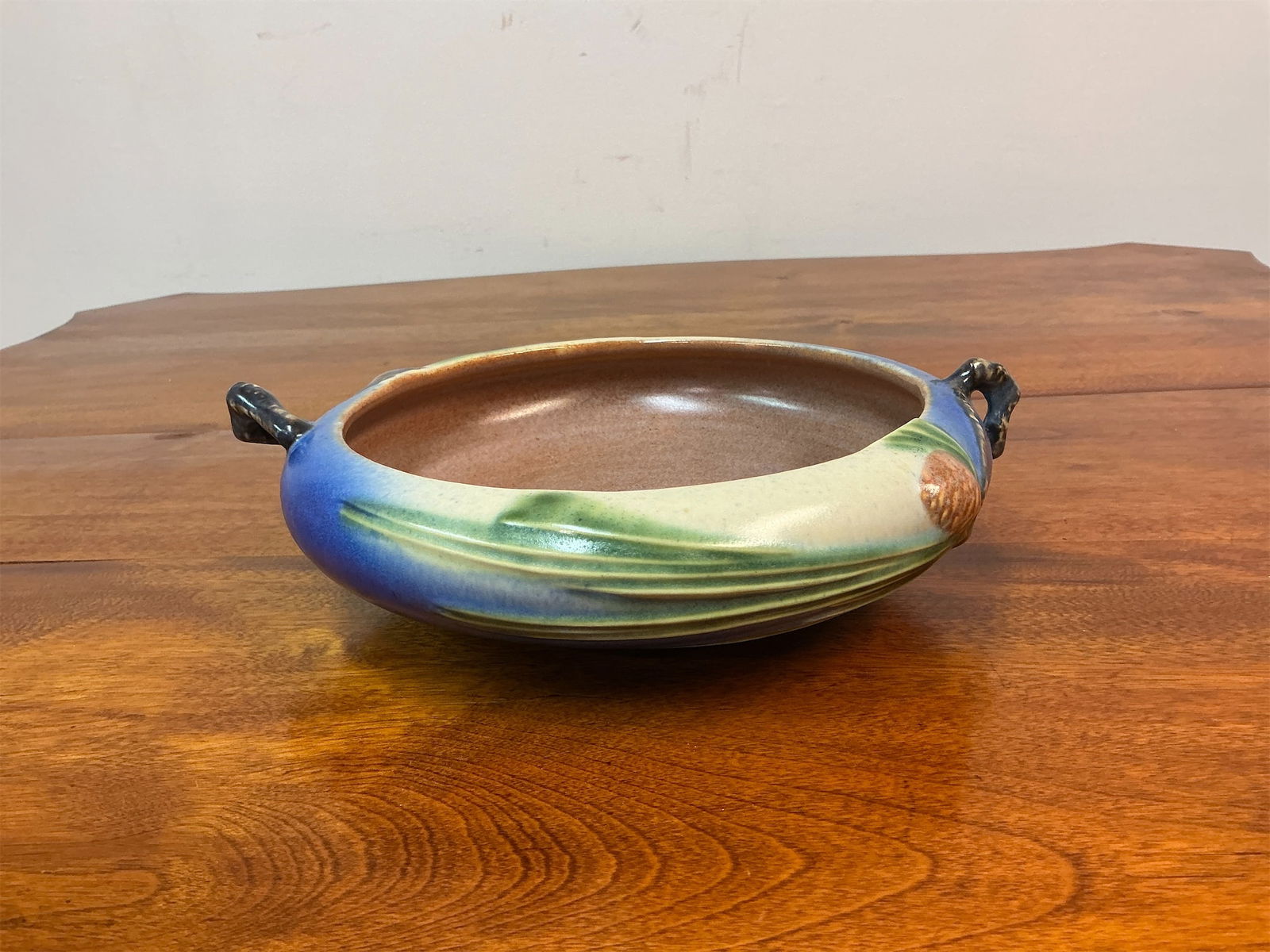 Roseville Pottery Blue Pincone Planter Bowl: Roseville Pottery Blue Pinecone Planter Bowl showcases a charming design with intricate details. The bowl features a rich blue glaze complemented by a delicate pinecone motif and stylized foliage, con