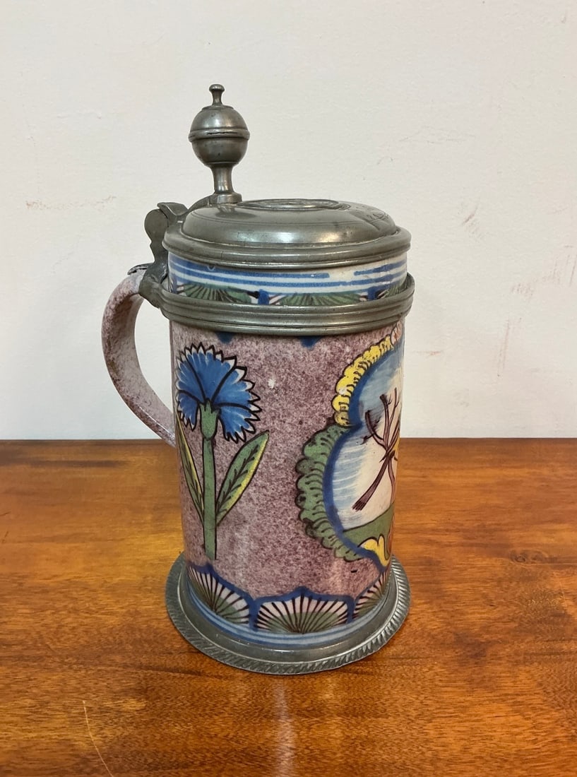 Antique German Faience Tankard: This exquisite antique German faience tankard showcases vibrant hand-painted floral designs with intricate details with tin lid and base and a charming bird motif. The body features a beautiful