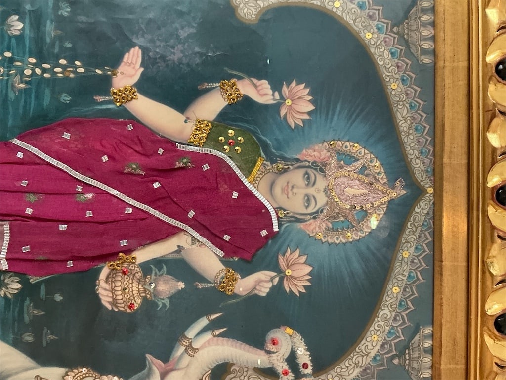 Framed vintage embellised print of Hindu goddess Lakshmi: This exquisite framed vintage print features the Hindu goddess Lakshmi, adorned in a vibrant maroon and gold outfit. The intricate detailing highlights divine elements, including her graceful posture 