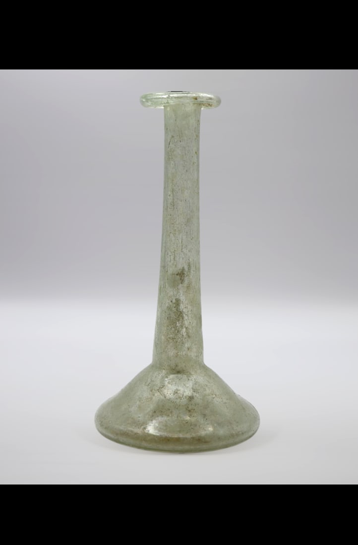 Roman Glass Perfume Bottle, Circa 1st Century AD: Colourless with light blue tinge. Lop-sided rim, folded out, over, and in, slightly flattened on top; tall cylindrical neck; squat bulbous body; flat bottom with slight concavity at centre. Intact; pi