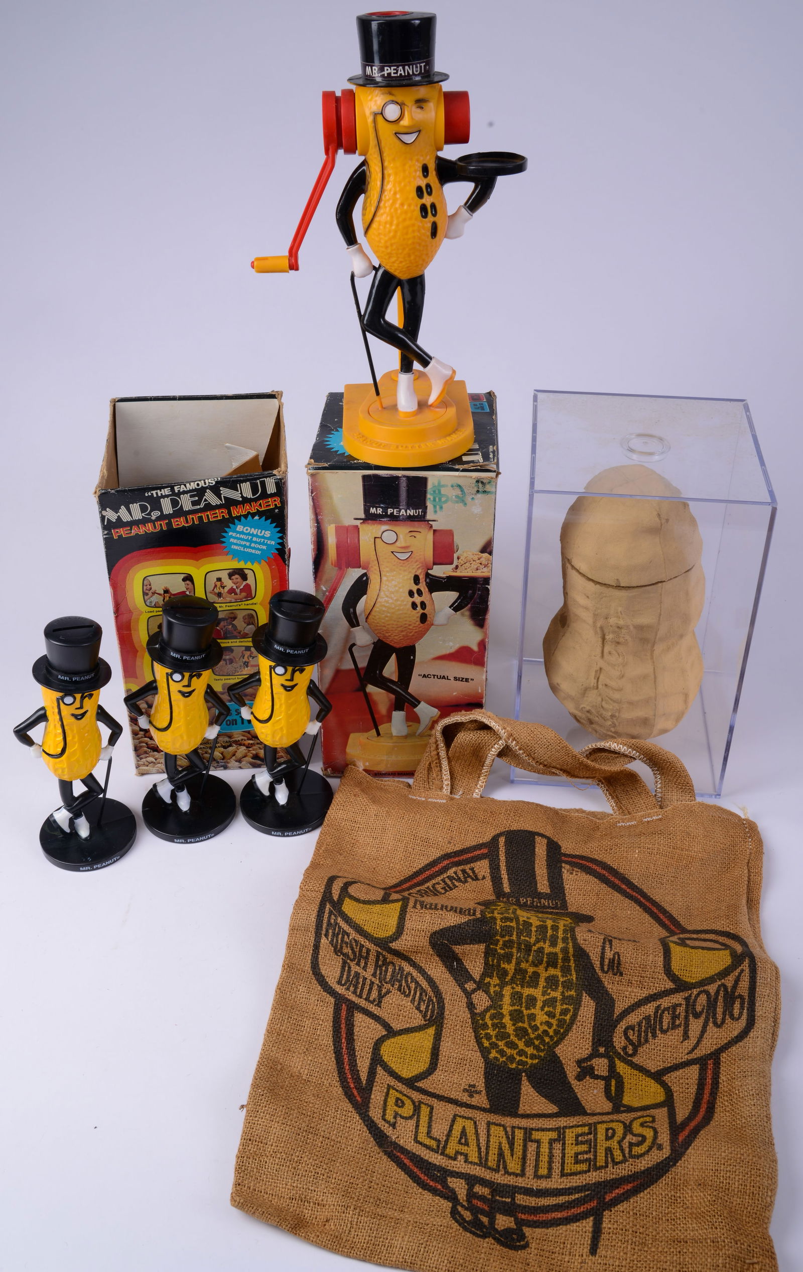 Planters Peanut Memorabilia: Including large peanut in case, 3 Mr. Peanut plastic coin banks, 2 Mr. Peanut peanut butter makers in original boxes and peanut bag. Height of peanut in case 12 inches.