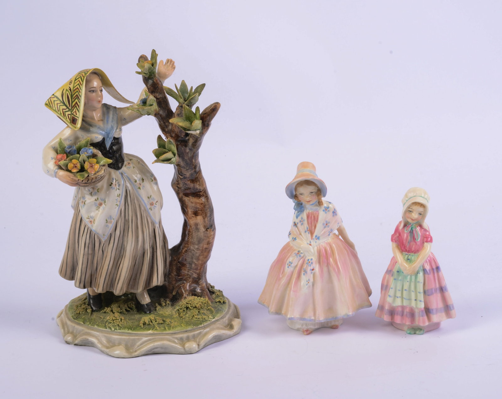 Three Porcelain Figures of Women.: One signed G. Tripi, height 9 inches, and two Royal Doulton. A few losses to larger example.