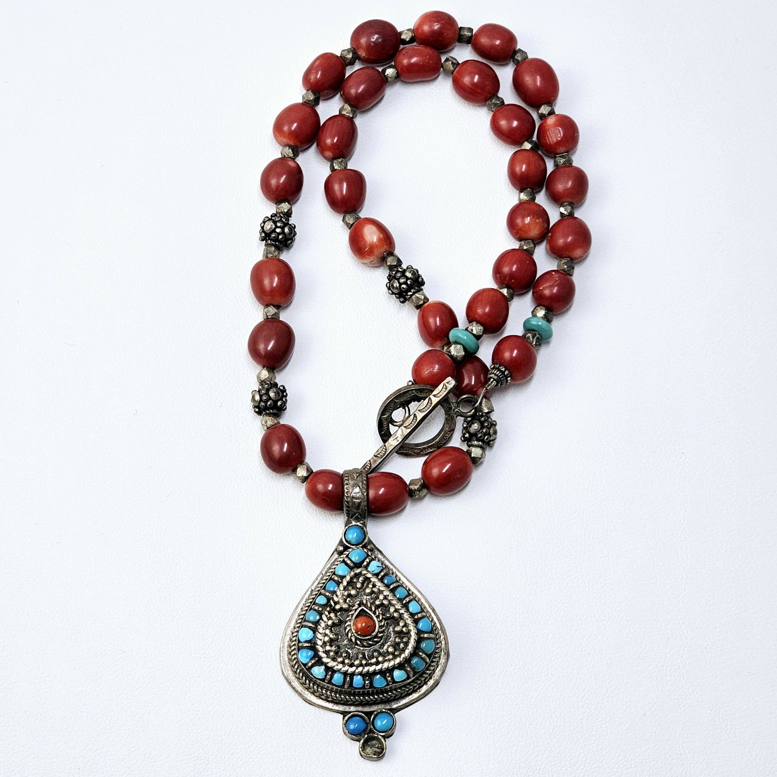 Tibetan Style Coral, Turquoise, and Sterling Necklace: Tibetan style necklace composed of barrel-shaped coral interspaced by silver and metal beads, terminating to a pear-shaped sterling silver pendant featuring coral and turquoise cabochons. Total length