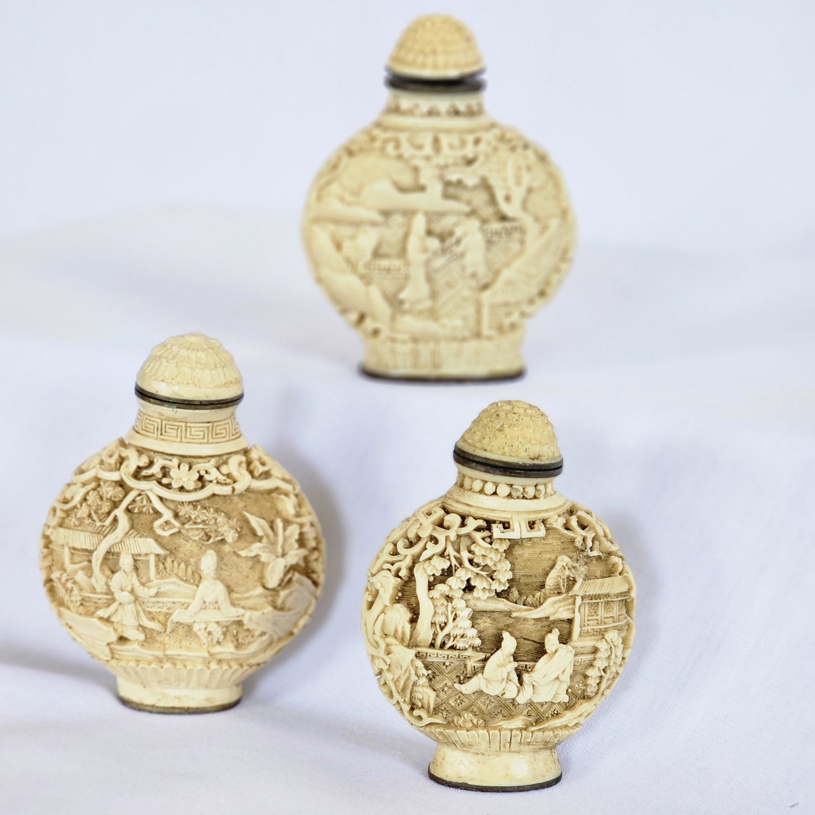 Three carved snuff bottles: Small cream-color carved snuff bottles with vignetted female or scholar figures in gardens