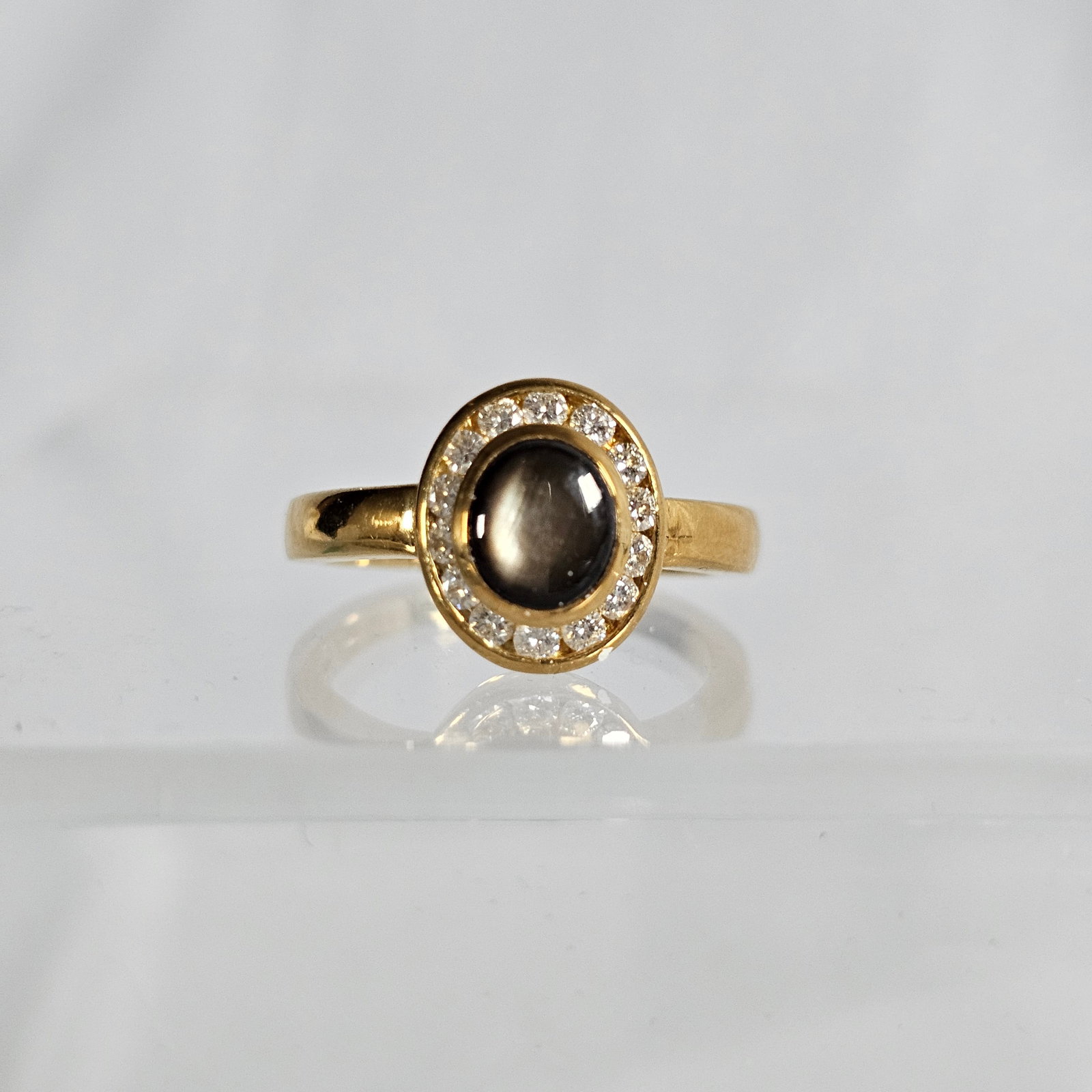 Black Sapphire, Diamond, 18k Yellow Gold Ring: Centering an oval-cut black sapphire cabochon measuring approximately 6.80 x 5.80 mm, highlighted by fourteen full-cut diamonds weighing a total of approximately 0.28 cttw., set in an 18k yellow gold 