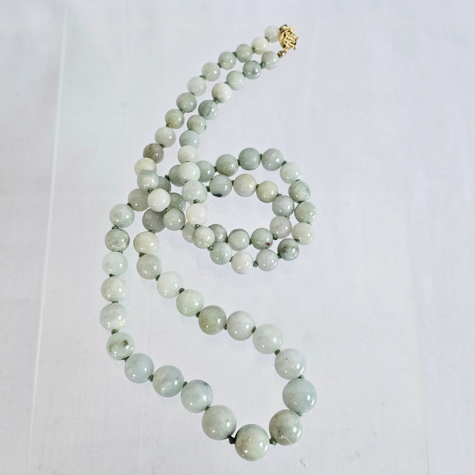 Graduated Jade, 14k Yellow Gold Necklace: Composed of seventy-four jade beads graduating from approximately 12.0 to 7.0 mm, completed by a 14k yellow gold, Asian motif hook and box clasp with safety arm, forming a 29 inch necklace. Gross