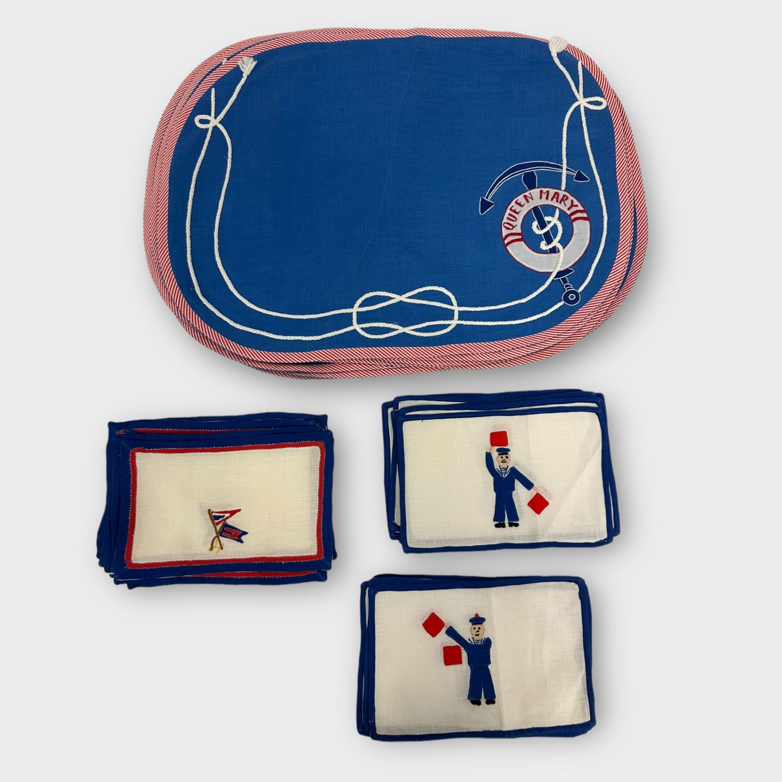 Group of Table Linens: Group of table linens including placemats with a life preserver around an anchor with the Queen Mary name on it and 3 groups of linens including flags and signaling that signifies "J" and &q
