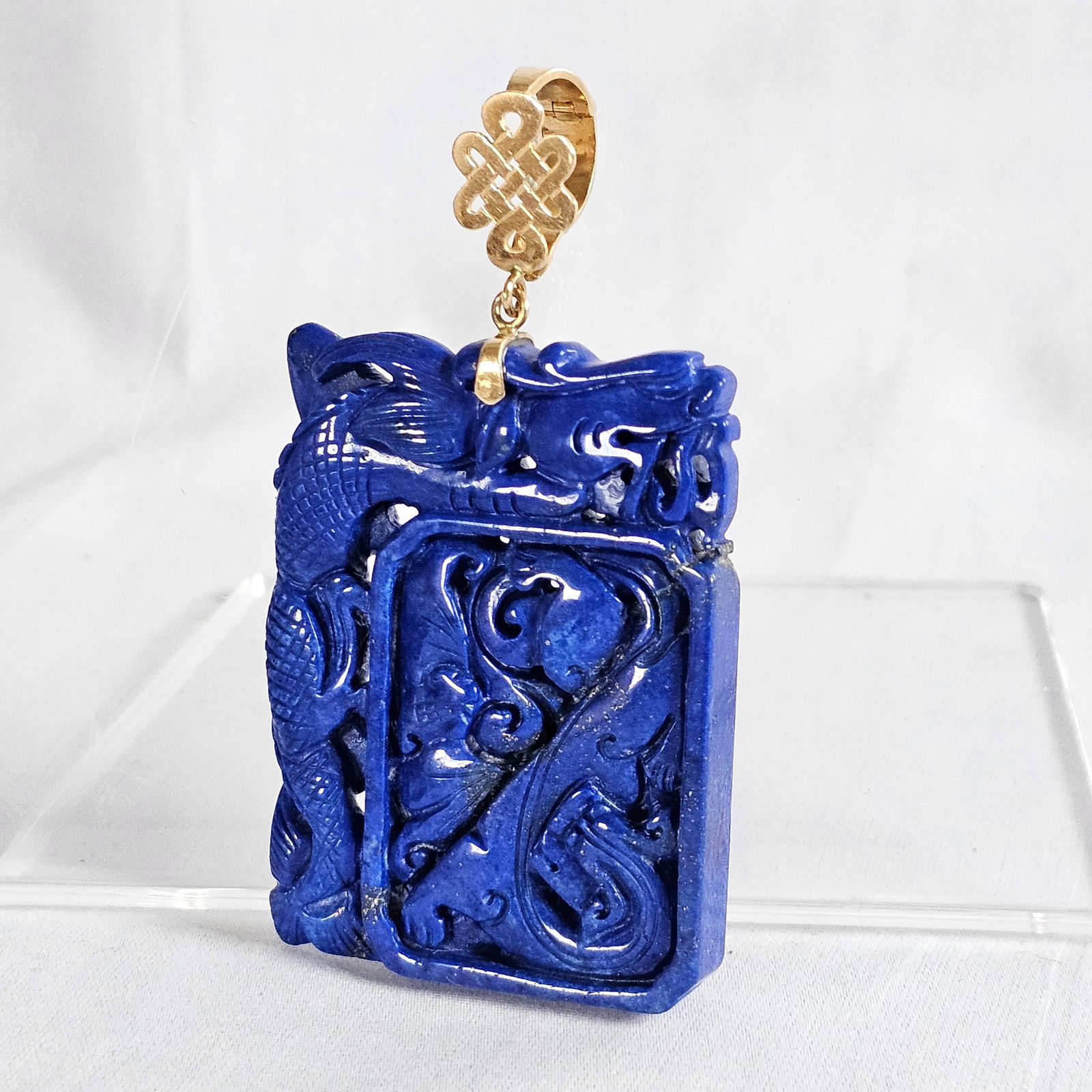 Carved Lapis Lazuli, 14k Yellow Gold Enhancer Pendant: Composed of a rectangular lapis lazuli plaque measuring approximately 58.0 x 44.0 mm (2.28 x 1.70 in), highly carved and pierced with flowers, birds and mythical beasts, suspended by a 14k yello