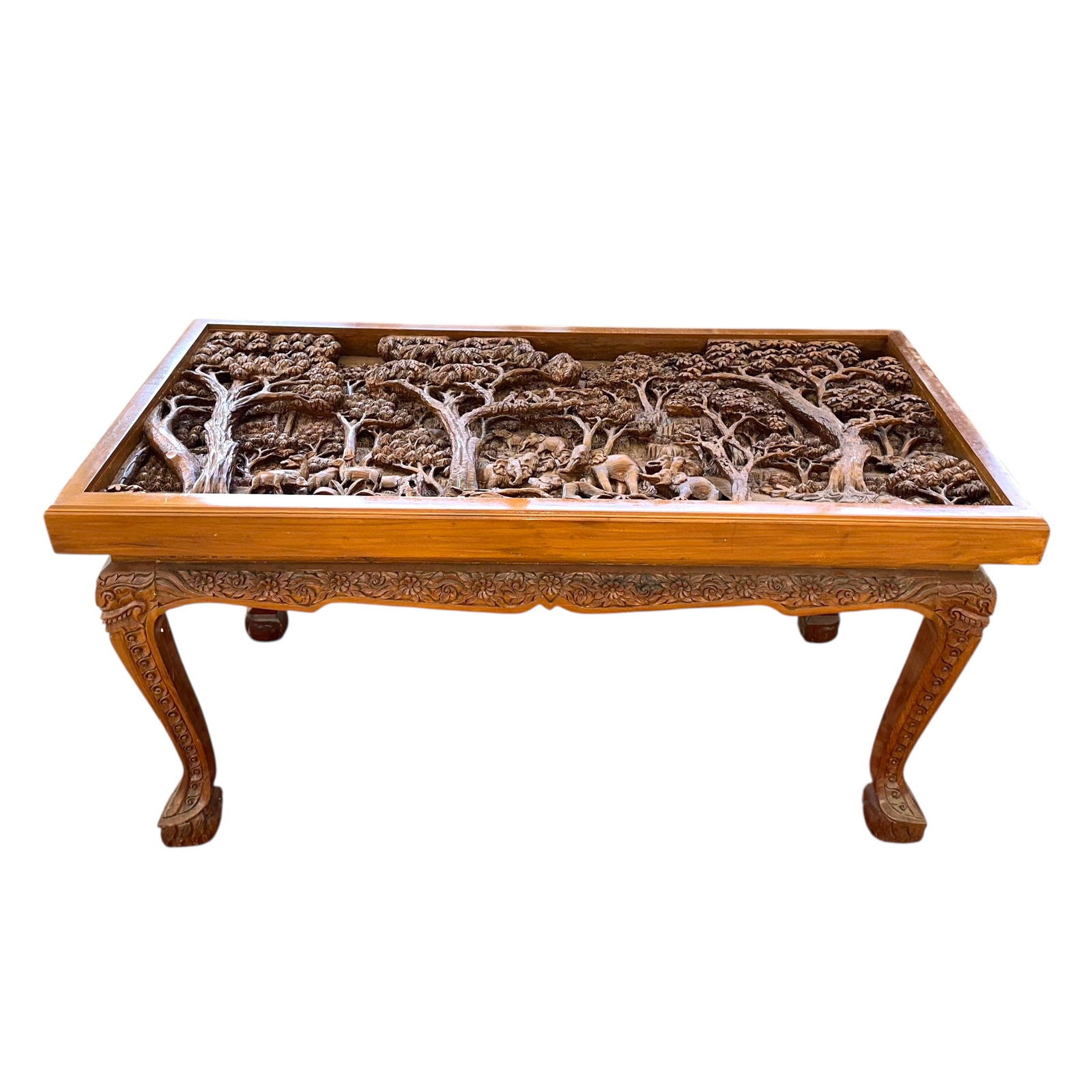 South Asian Carved Hardwood Dining Table: A South Asian carved hardwood dining table. The rectangular top relief carved with a scene depicting a herd of elephants in a jungle clearing beneath palm and exotic fruit trees above a flowing stream