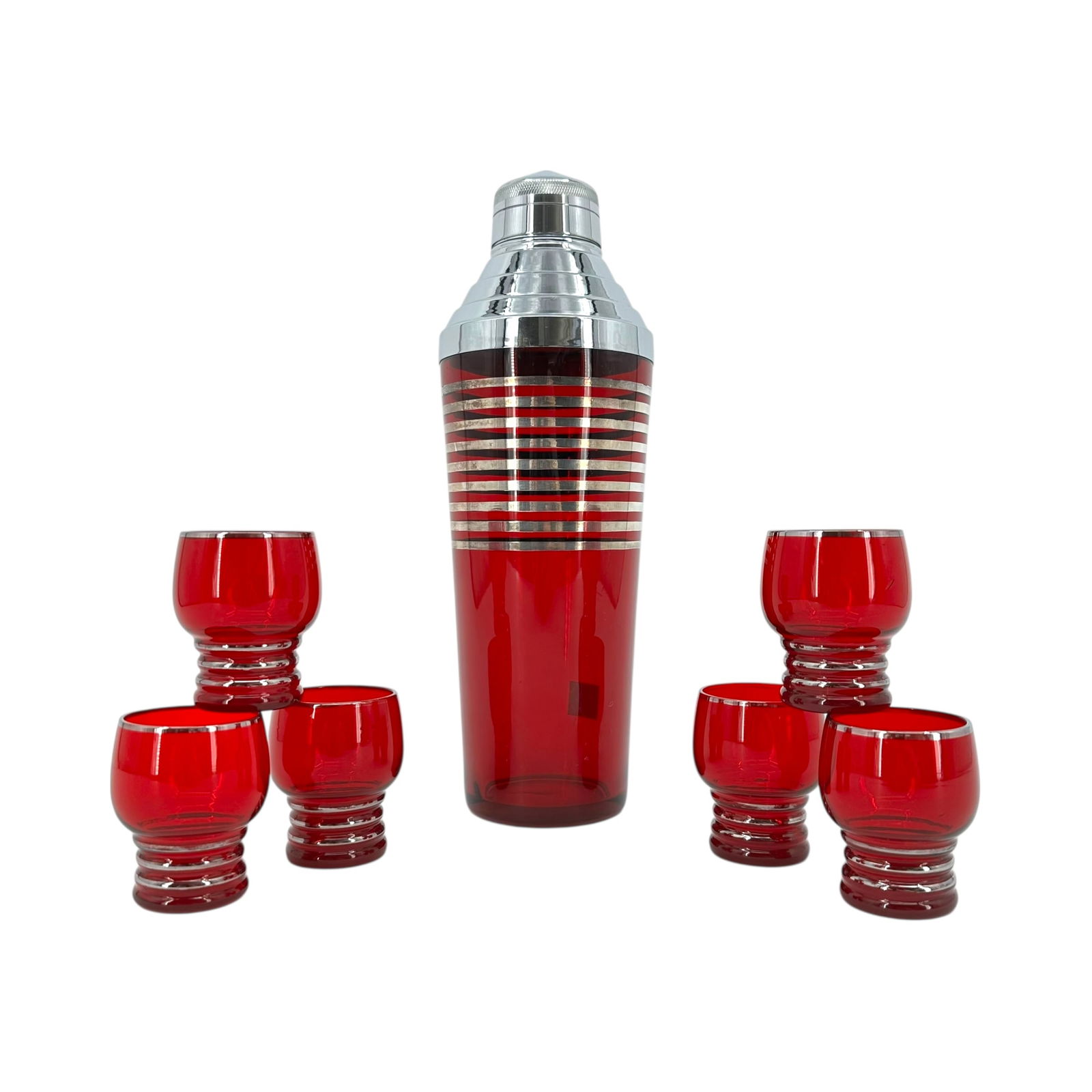 (Lot of) 7 Pcs: Ruby Glass Cocktail Shaker and 6 Glasses: (Lot of) 7 pcs: a MCM ruby glass cocktail shaker with silver tone bands along with 6 footed glasses with silver tone bands. Glasses measure approximately 2 1/2 in tall and shaker measures approximatel