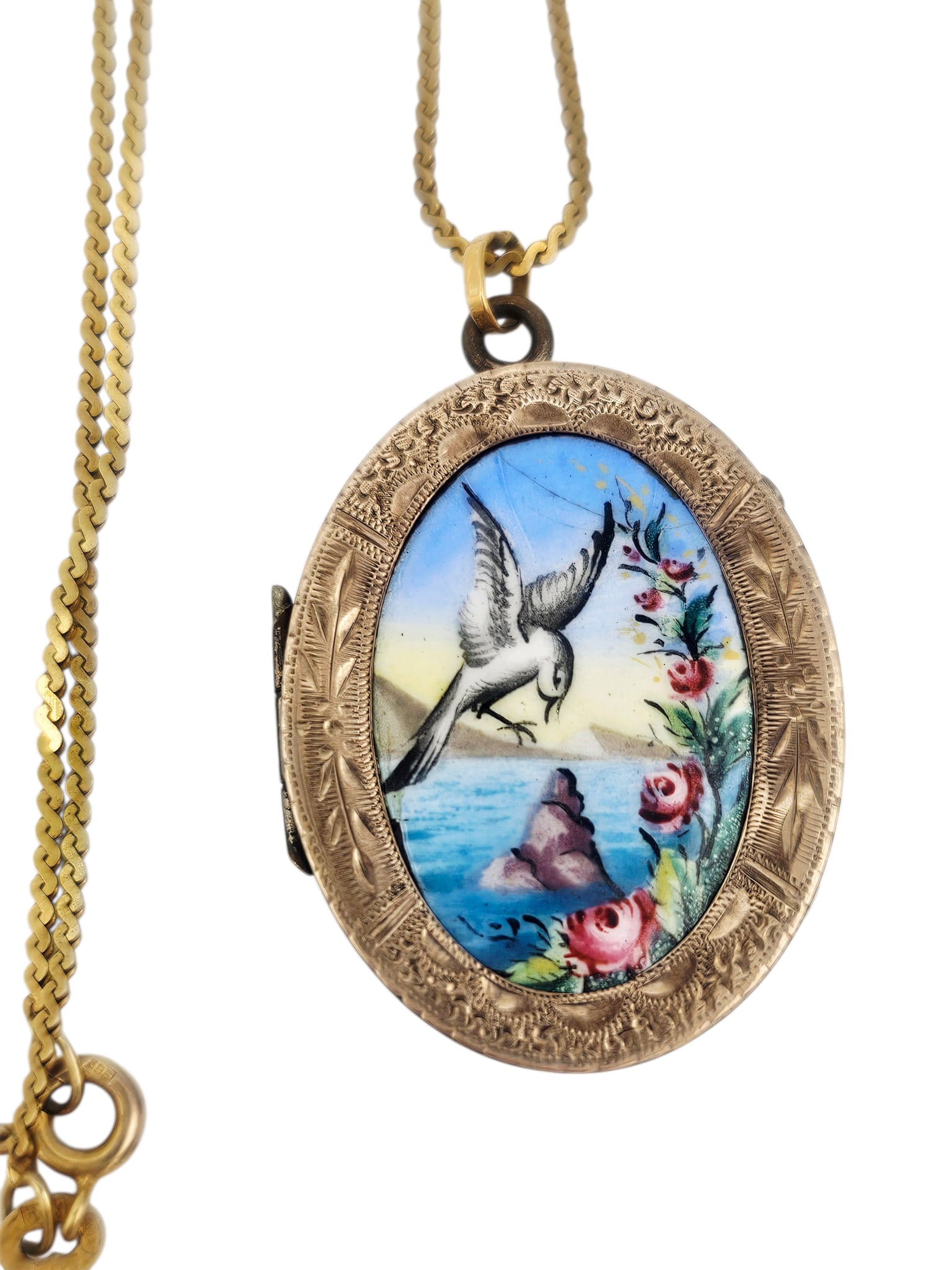 Victorian Enamel, 10k Locket with 14k Chain: Centering an oval enamel plaque depicting a bird in flight within a lakeside landscape, set in an engraved, 10k yellow gold locket measuring approximately 1.40 x 1.00 inches, foliate engraving to the