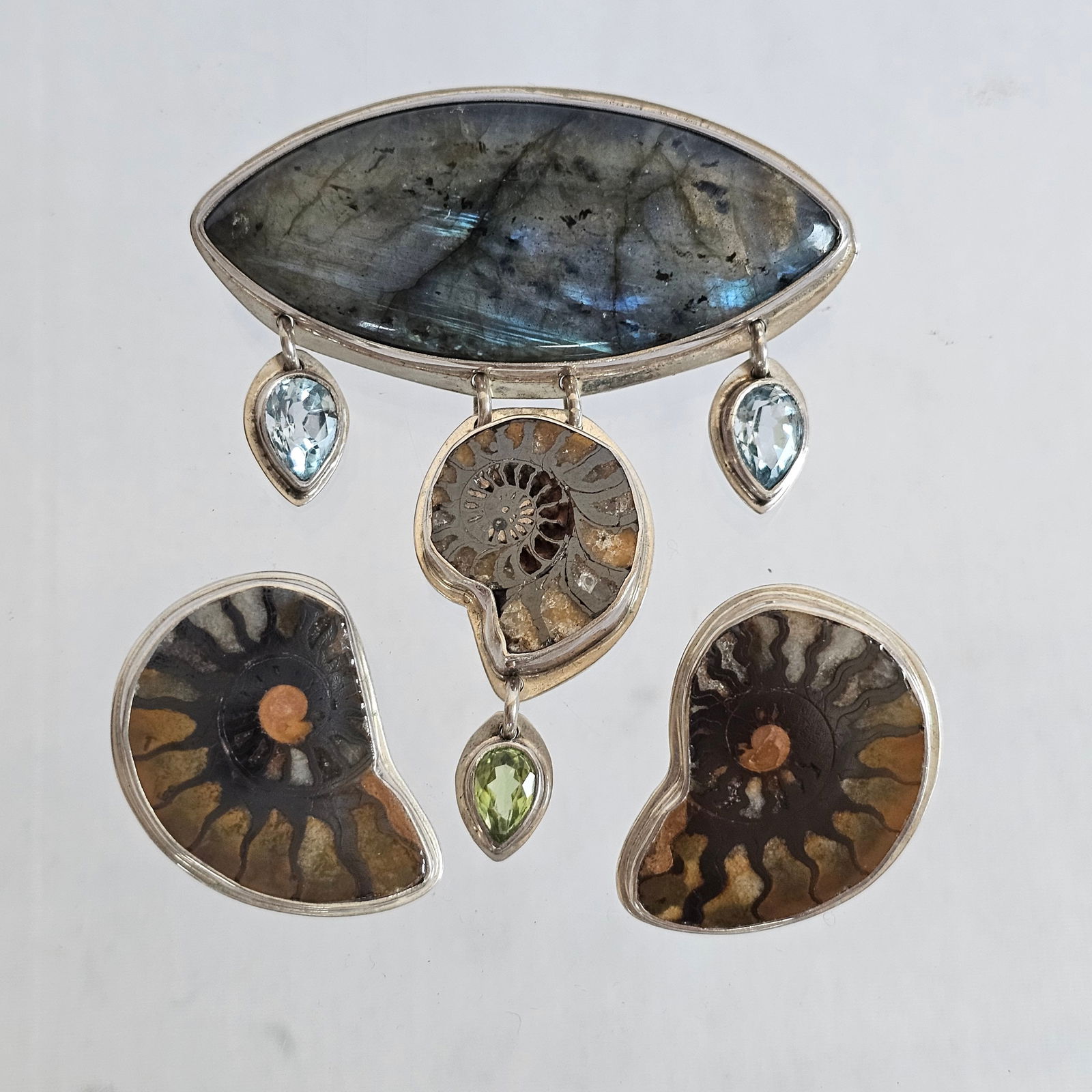 Ammonite, Multi-Stone, Sterling Studio Jewelry Suite: Including a pin featuring a navette-shaped labradorite cabochon suspending an ammonite, two pear-shape blue topaz and one pear-shape peridot set in a sterling silver mounting measuring approximately 6