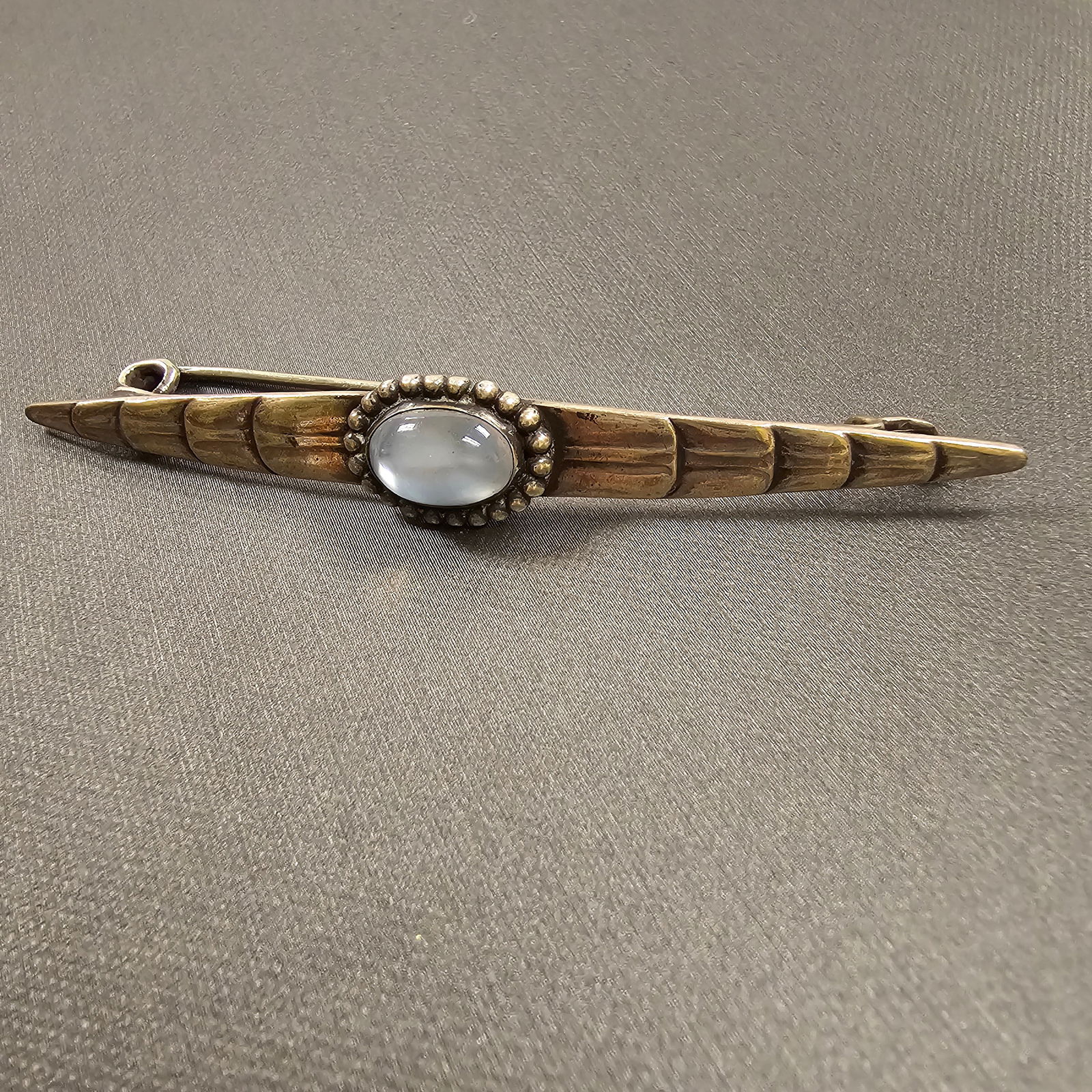 Early Georg Jensen Moonstone, Silver Bar Pin, 115: Centering an oval moonstone cabochon measuring approximately 12.74 x 8.31 mm, set in an 830 silver bar pin mounting measuring approximately 3.30 x 0.50 inches. Gross weight: 9.0 grams. Marked: GI 830