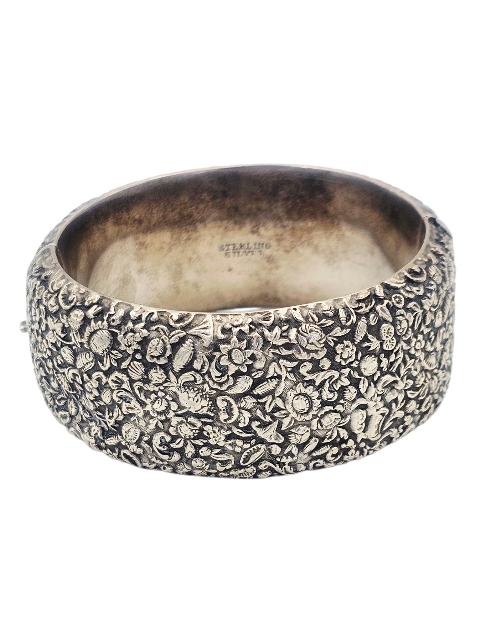 Victorian Sterling Silver Bracelet: Featuring repousse flowers, set in a hinged, sterling silver bracelet mounting measuring approximately 1.23 inches in width, completed by a hidden push-button tongue-and-groove clasp fitting to 7