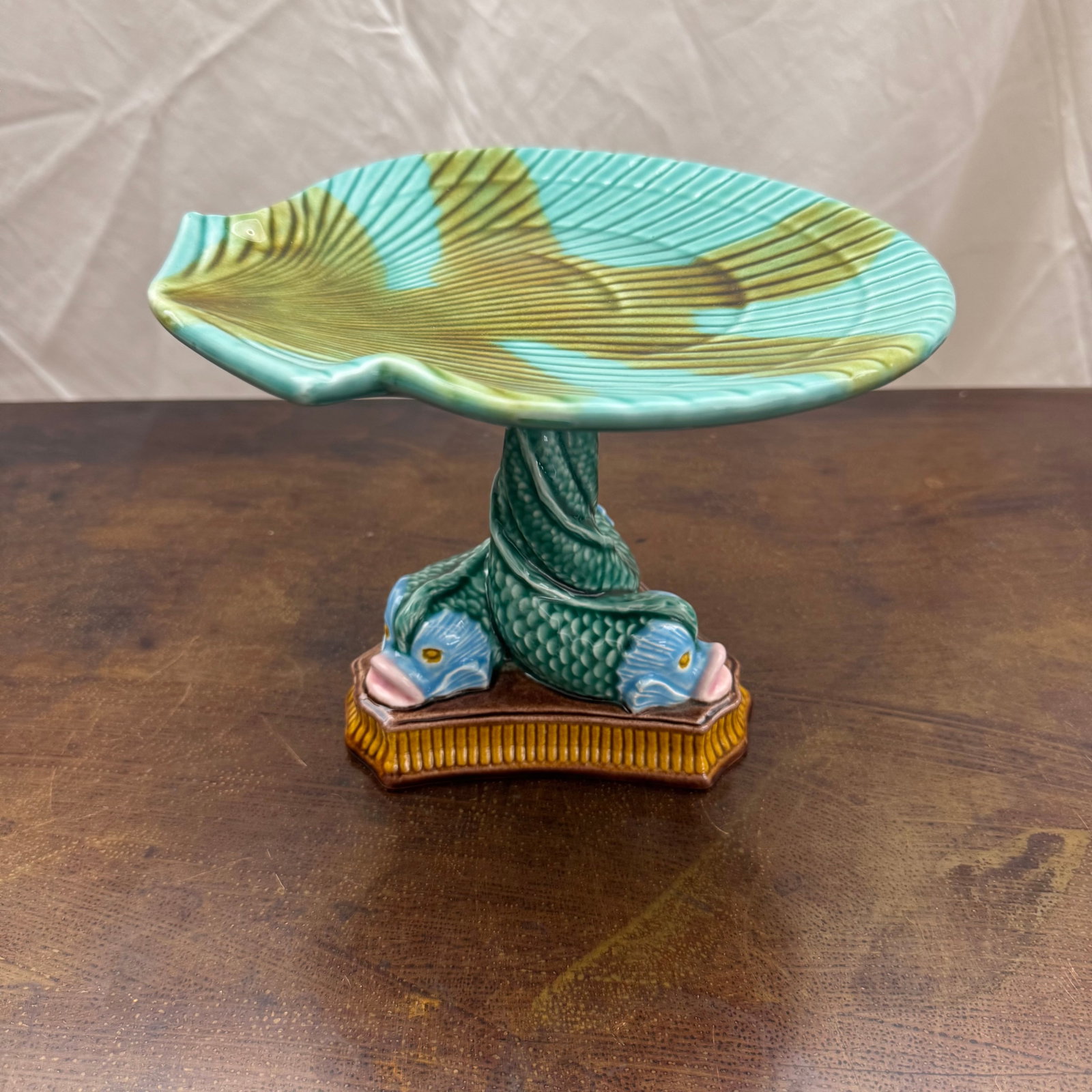 Zrike Pottery Shell Serving Plate with Fish Stand: Zrike Majolica style pottery featuring a shell serving plate on an ornate fish stand with intertwined fish.