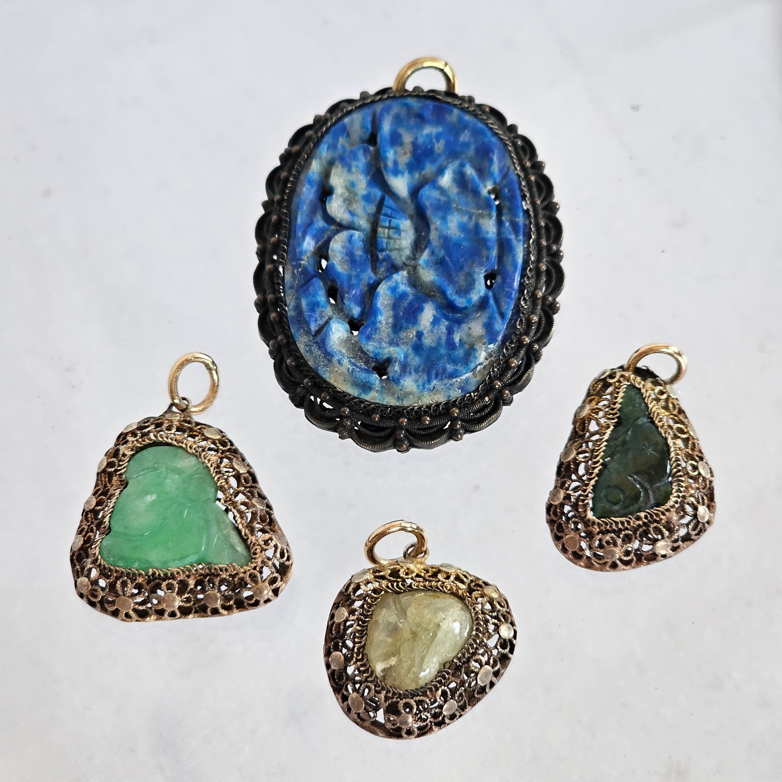 Collection of Chinese Export Multi-Stone Pendants: Including two carved jade plaques and one tumbled citrine set in silver gilt pendant mountings measuring from approximately 20.5 x 21.0 mm to 19.0 x 17.0 mm, together with one carved sodalite plaque s