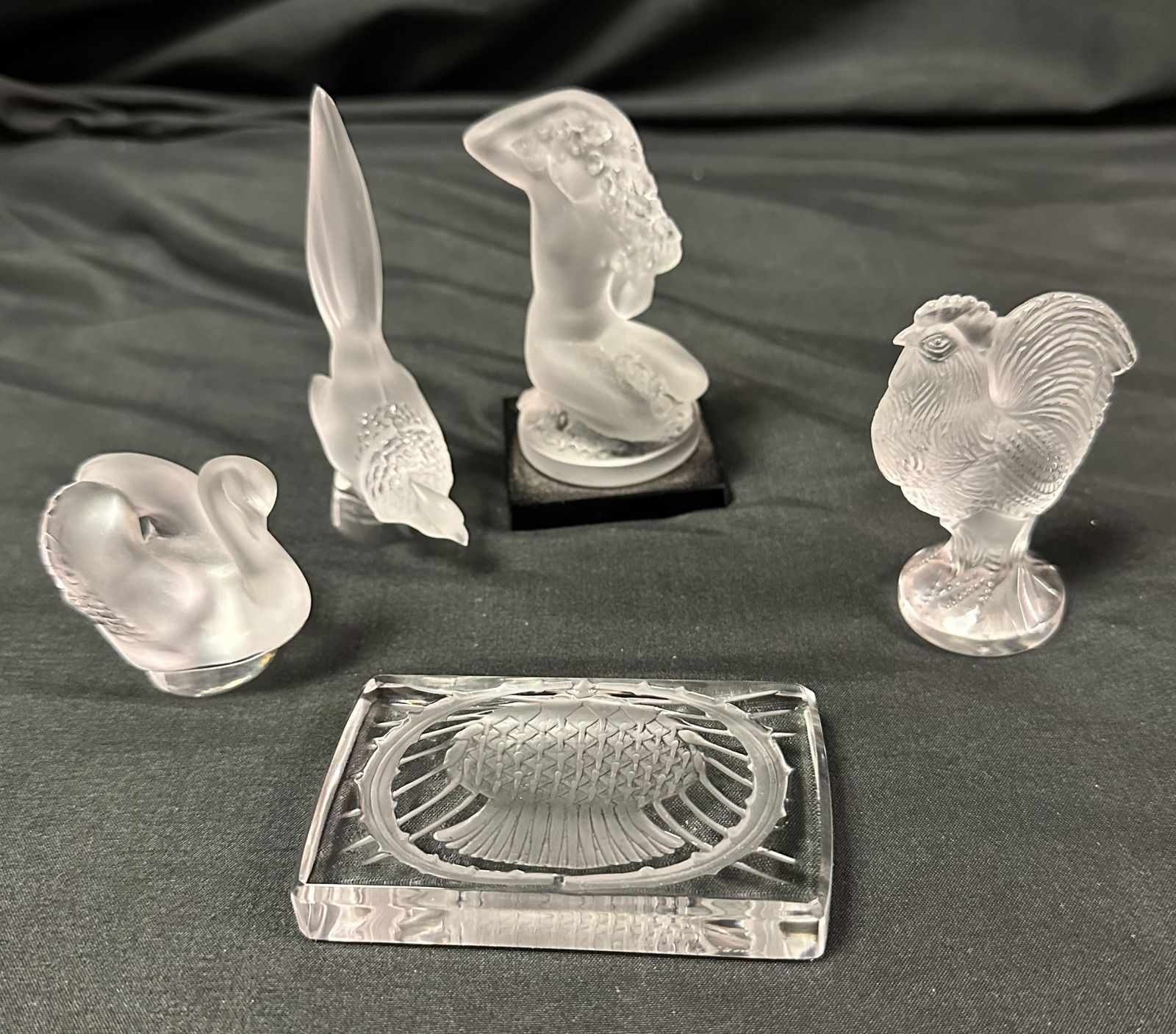 Four Lalique Figural Pieces and a Paperweight - III: Group of four Lalique figural pieces plus one rectangular paperweight. Group includes a swan, a pheasant, a posing nude on a black base and a rooster with the rectangular paperweight showing a thistle