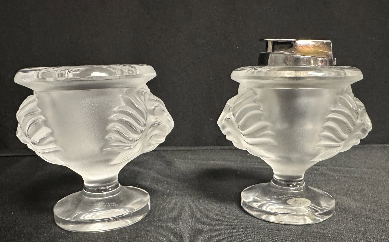 Lalique Tete de Lion Lighter and Cigarette Holder: Great set by Lalique. A Tete de Lion vessel holding a Ronson lighter (still sparks! Needs gas) original to the piece as indicated by the stickers on the bottom. The other frosted Tete de Lion is a com
