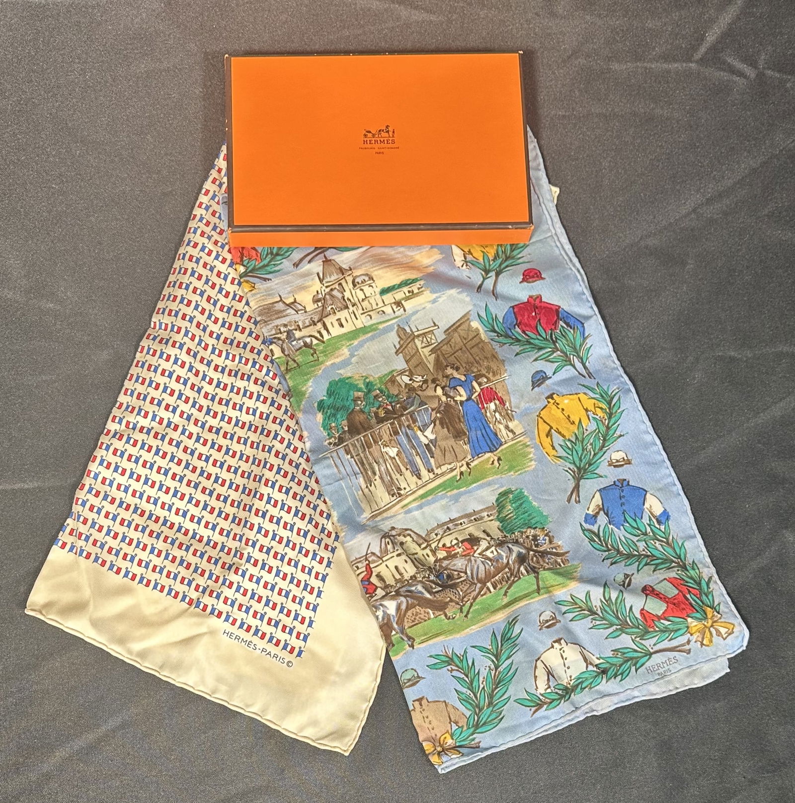 Hermes Two Pocket Squares in Box: Two Hermes pocket squares, one with a with a large array of French flags and the other with the Chantilly horse race print. These pieces have the well known hand rolled and stitched edges and the Flag