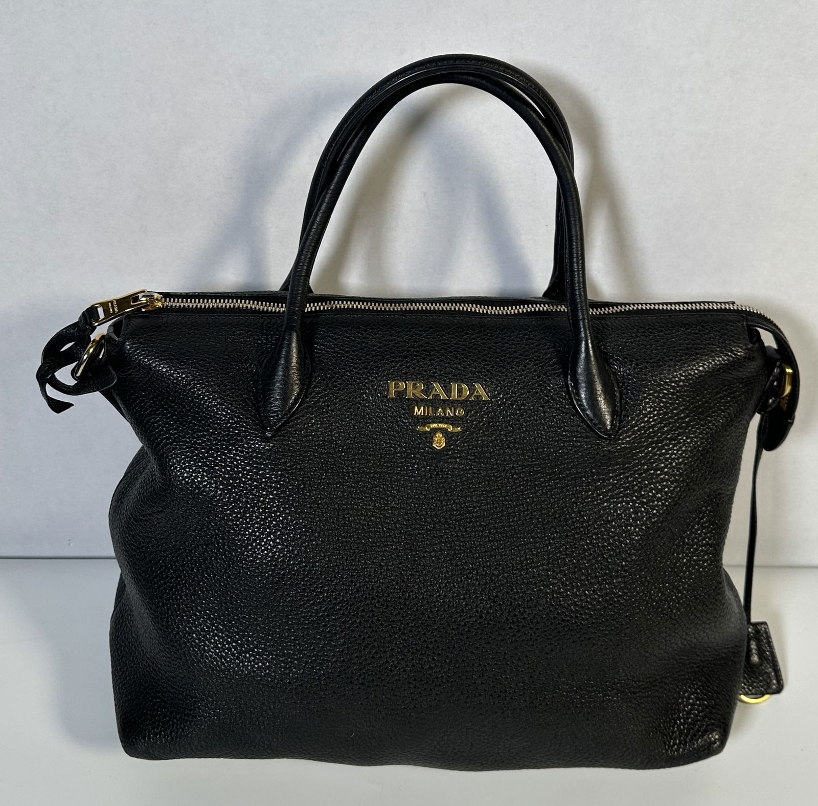 RR- Prada Vitello Daino convertible tote bag in black leather: Prada Vitello Daino convertible tote bag in black leather >Pre-owned Prada black Vitello Daino 2Way bag featuring dual rolled top handles, Saffiano leather, gold tone logo plaque hardware on front and