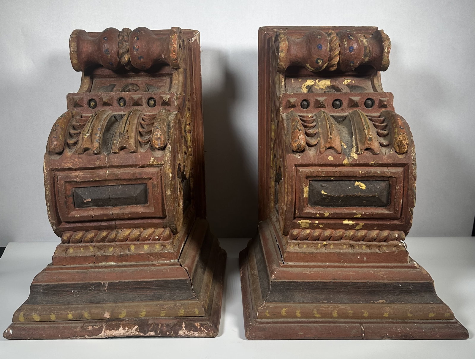 Wood Carved Large Painted Corbels: Wood Carved Large Painted Corbels This pair of antique architectural wooden corbels features intricate hand-carved acanthus leaf details, a scrolled volute, and weathered red polychrome paint. For thi