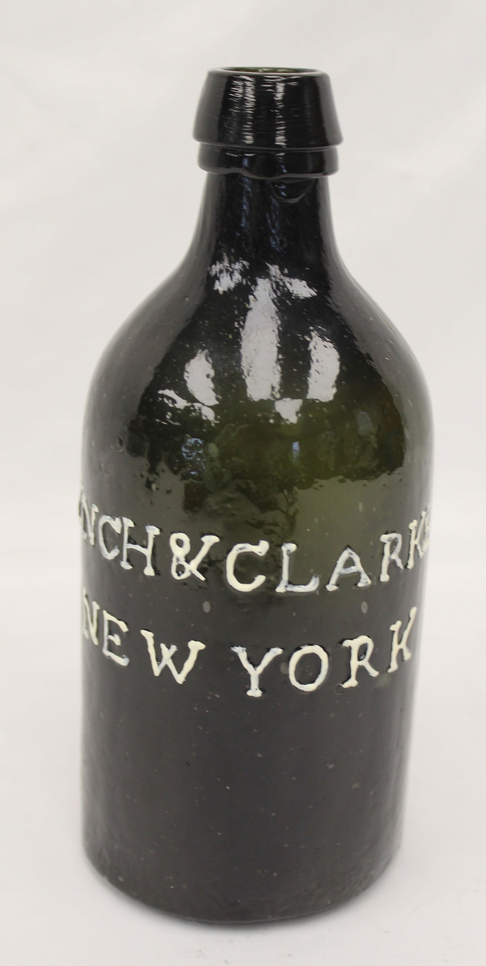 Early dark olive green glass bottle "Lynch & Clarke New York" raised decoration - 7 1/2" tall: Early dark olive green glass bottle "Lynch & Clarke New York" raised decoration - 7 1/2" tall
