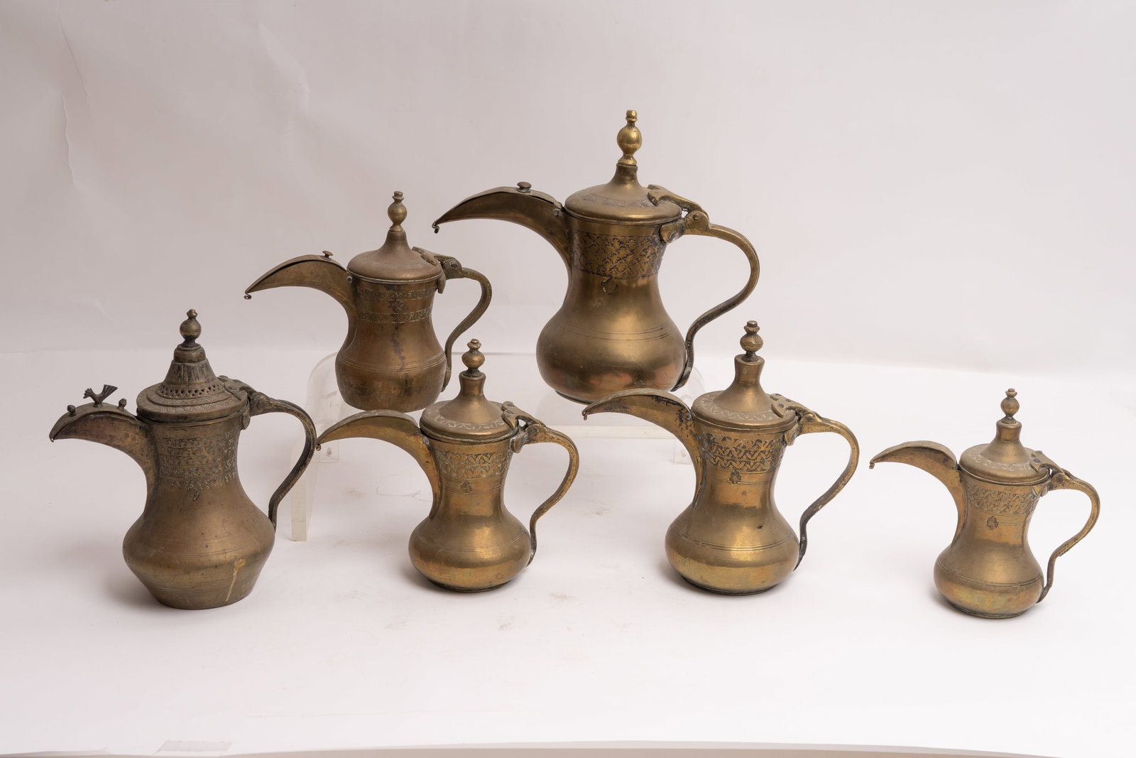 Grouping of Six Middle Eastern Antique Islamic Arabian Dallah Coffee Pots.: Three appear to be a matching set and the others are all different, but all have maker stamps. Each has a weighted lid. The largest pot measures 12" with the handle and spout x 11"H. Smallest measures