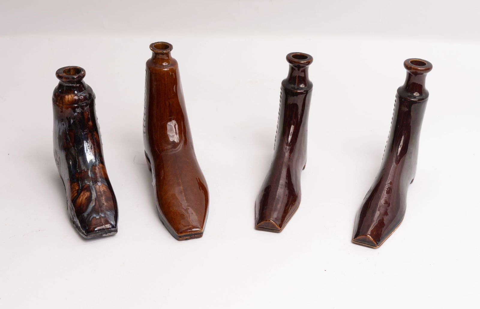 Grouping of Four Rockingham Pottery Shoe Flasks.: Two are a matching pair and measure 7" long x 6" high and one has a small glaze chip at the back side of the lip. The light brown shoe measures 8" long x 6-3/4" high and has chips at the top lip. The