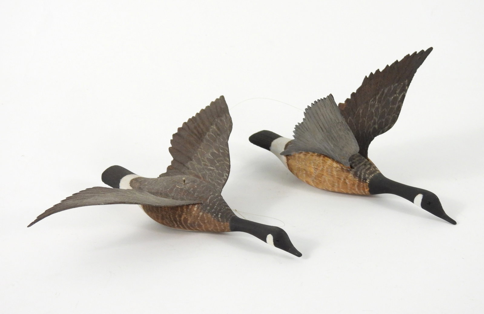 PR Carved Wood Canadian Geese Sculptures: United States, 20th Century. Includes two carved wood Canadian geese frozen in flight. From the collection of a Princeton, Massachusetts estate. Smallest 4" t x 7 1/4" w x 5" d, Largest 2" t x 7 1/4" 