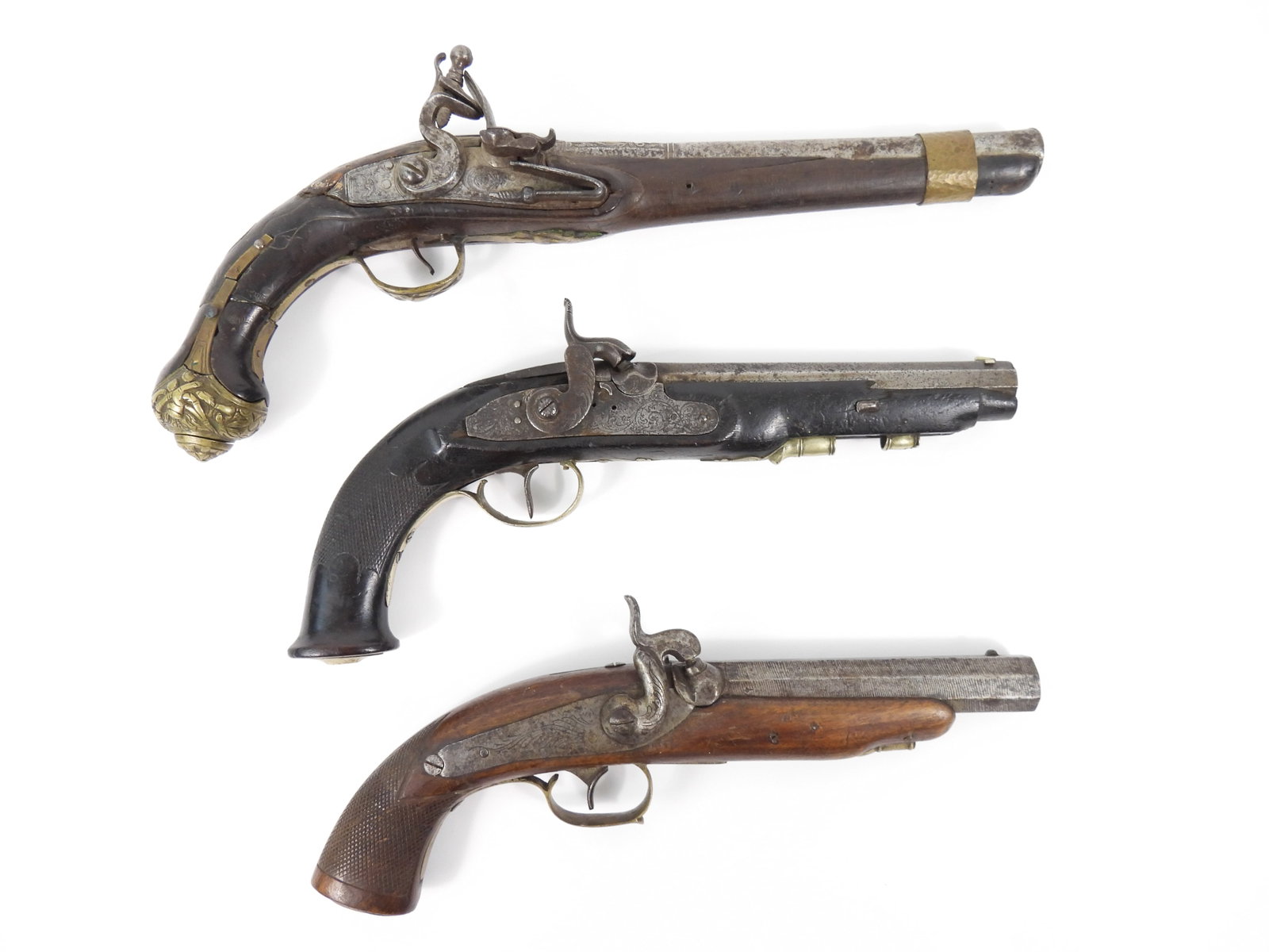 Three Early Pistols: A flintlock pistol made for Middle Eastern use with a cracked wrist and some wood losses, lock engraved with a moon and foliate designs, brass fittings, and an engraved breech; a Belgian or French per