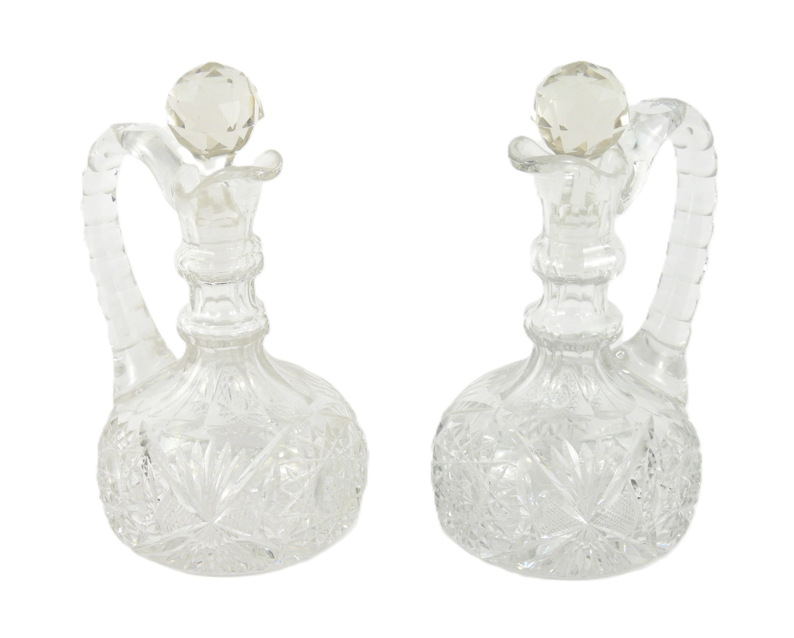 PR Cut Glass Cruets: United States, 20th Century, Glass. Pair of clear cut glass cruets with faceted stoppers and star patterns to body. Each approx. 7 1/2" x 4 1/2" dia.