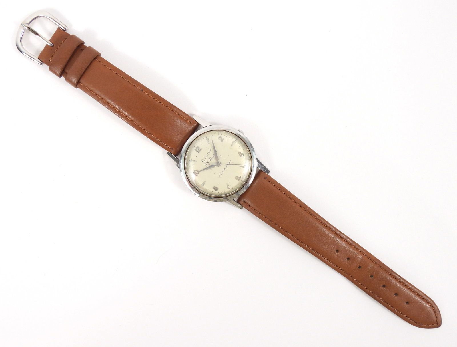 Mid Century Men's Bulova Self Winding Wrist Watch: Switzerland, Mid 20th Century, Metal, leather. Round metallic cream face with silver Arabic numeral and line numbering on a tan leather strap. Strap overall 9 1/8" long