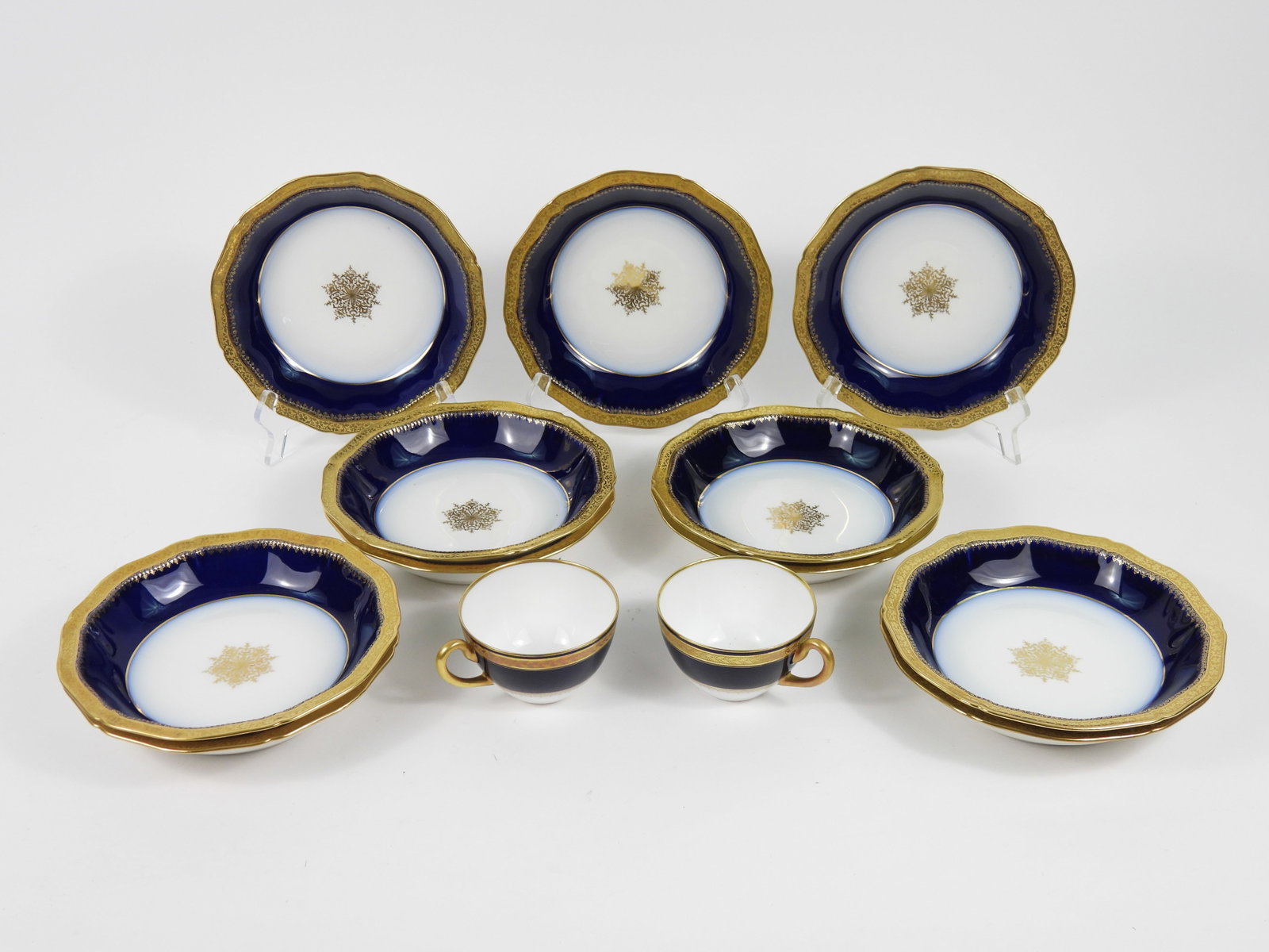 13PC Haviland & Hutschenreuther Porcelain Ware: France, Germany, Early 20th Century, Porcelain. Includes eleven Haviland bowls with central gilt botanical medallion surrounded by a cobalt blue and gilt rim, and a pair of Hutschenreuther teacups wit