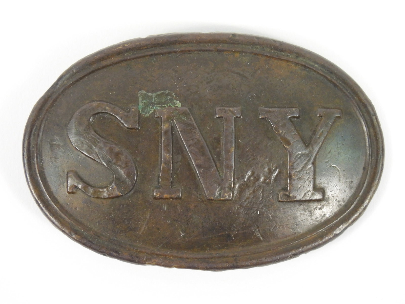 Dug State of New York Belt Plate: United States. Lead-filled brass plate marked "SNY"on face with two puppy paw-style attachment tabs on the back and a brass tongue.