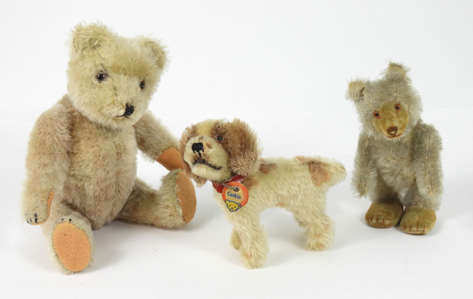 3PC Steiff Cockie & Other Mohair Bears: Germany, 20th Century, Mohair. Includes a Steiff "Cockie" with red collar, a mohair bear with gray fur and tan face, and a blonde mohair bear with brown glass eyes. Smallest 4" t x 4 1/2" w x 2 1/4"