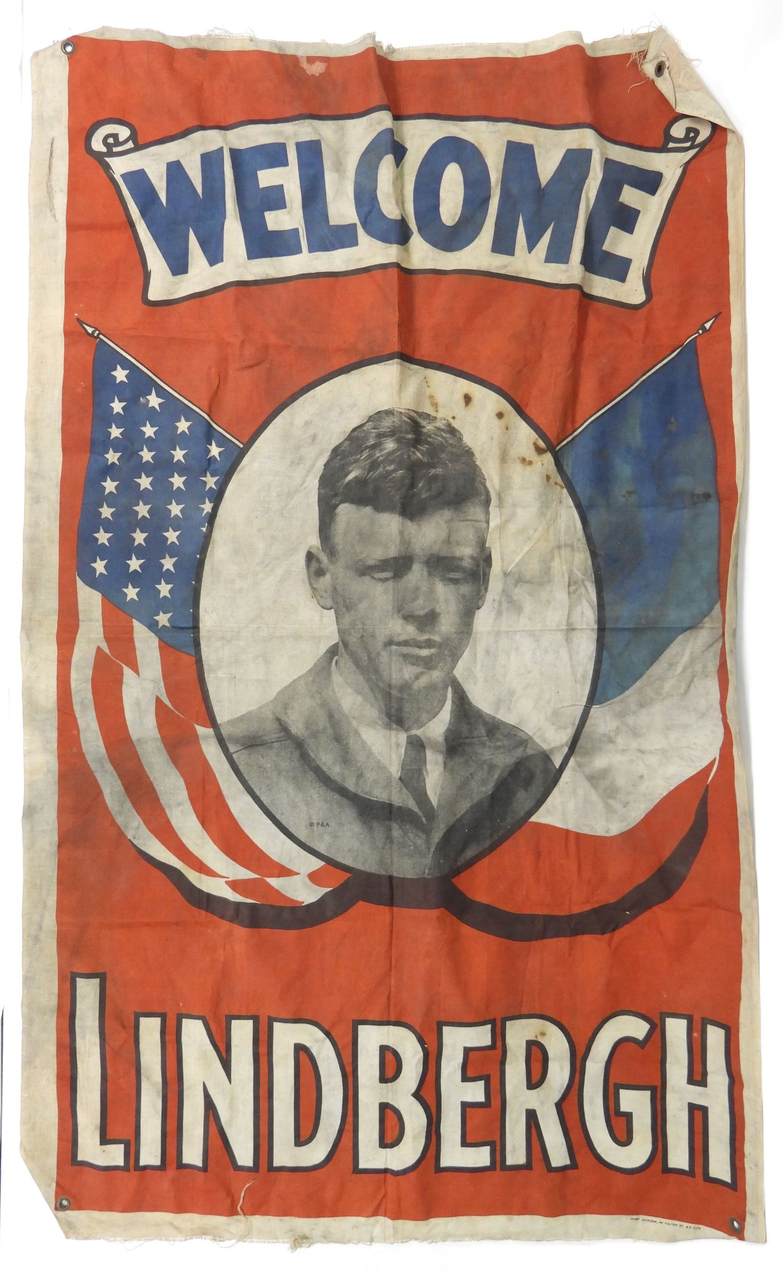 Charles Lindbergh Welcome Banner: United States, 1927, Textile. Banner depicting Charles Lindbergh flanked by American and French flags against a red background marked "Welcome Lindbergh." Charles Lindbergh was the first man to fly