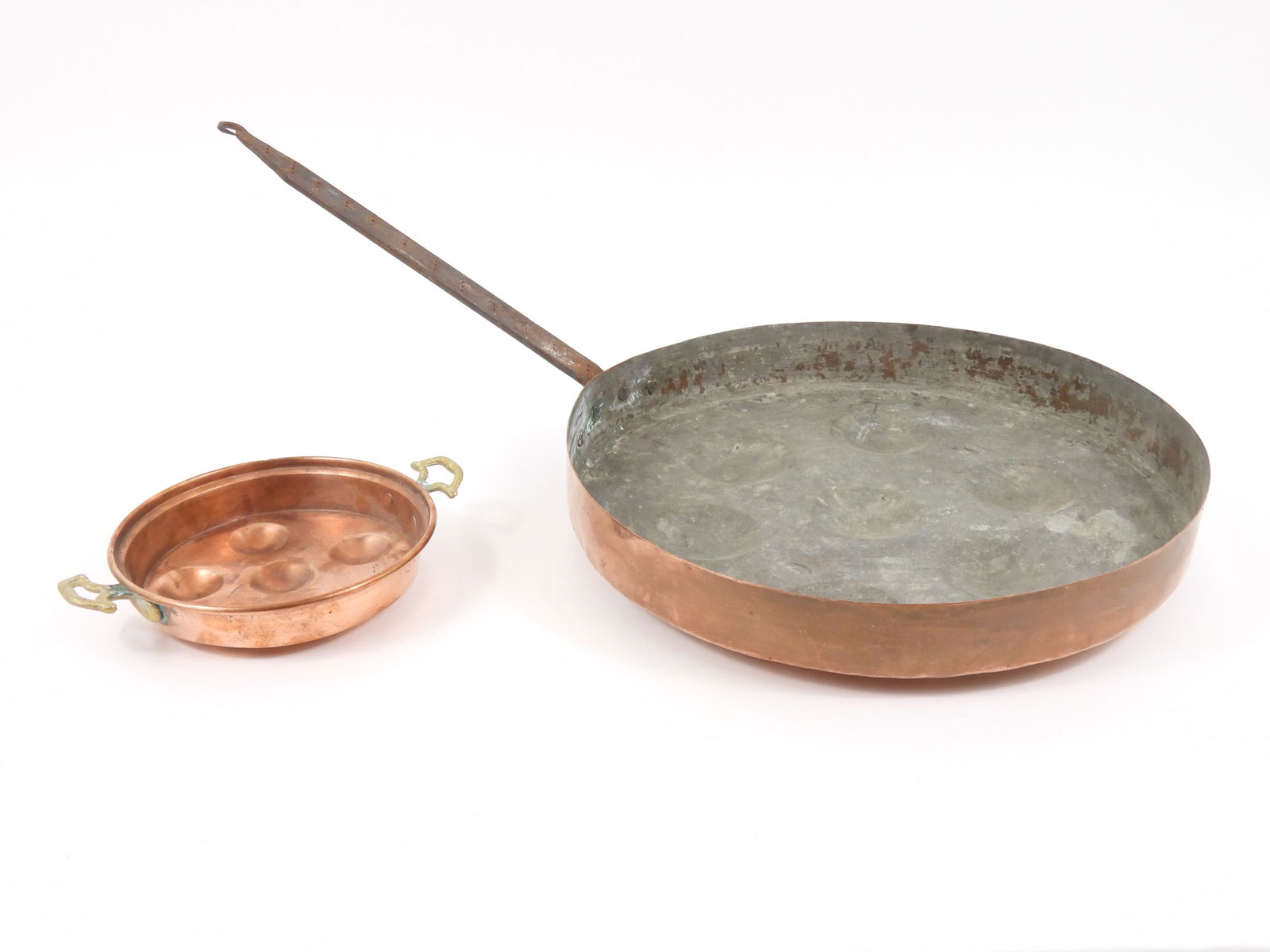 2 Antique Copper Poacher Pans: Includes a large hand made seven serving poaching pan with wrought iron handle measuring 2 1/4" x 15 1/4" dia., overall 28" long with handle; and a small 1 3/4" x 7 1/4" six serving escargot type