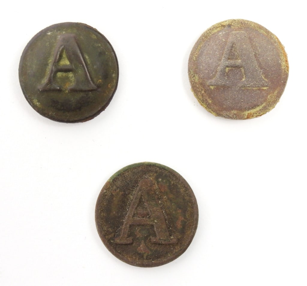 Three Dug Confederate Artillery Buttons: A coat-size block "A" artillery button with a missing shank and no visible back mark (22.6mm); a coat-size block "A" button missing the shank and still filled with dirt (23.2mm); and a coat-size block