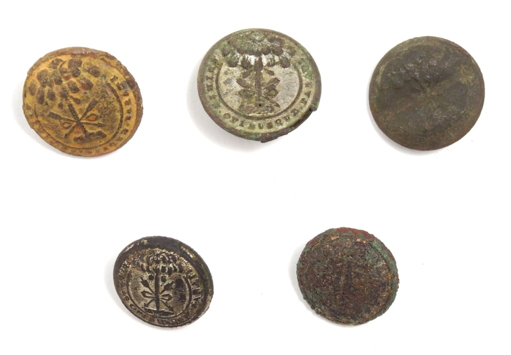 Five Dug South Carolina Buttons: A coat-size South Carolina button with an intact shank and illegible back mark (22.2mm); a coat-size flattened South Carolina button with remnants of silver wash, with an intact shank and "NEW YORK"