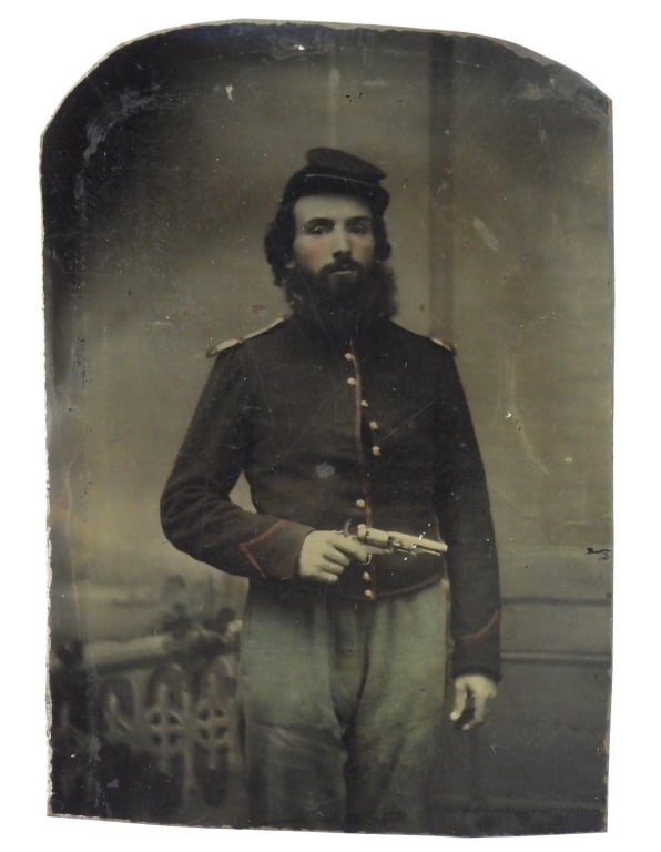 Civil War Tintype of a Soldier with Revolver: Image of a bearded soldier wearing a mounted services jacket with brass shoulder scales, a kepi, and sky blue trousers with a cocked pocket revolver in his hand. United States C. 1861-65 Ht. 3 5/8"
