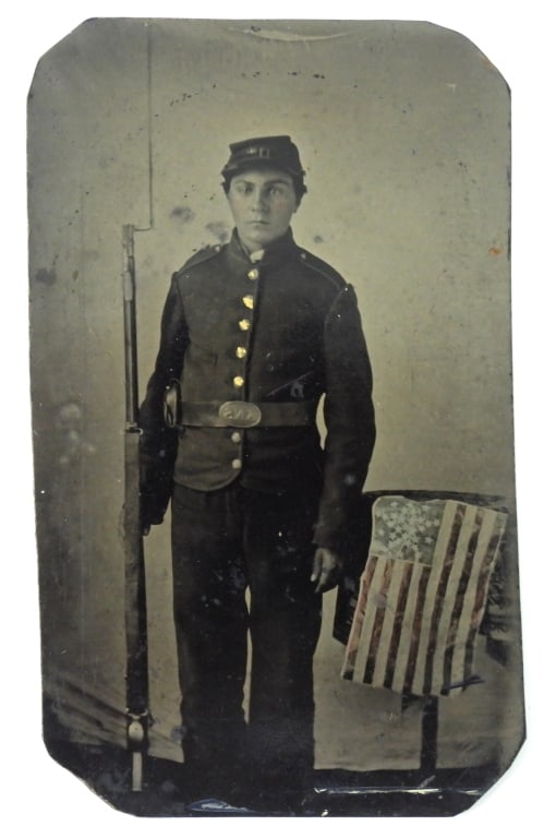 New York Soldier Tintype with Arms and Flag: A soldier wearing a New York State jacket and kepi, an SNY buckle and cap box on his belt, armed with a musket and bayonet, with a star pattern flag next to him. United States C. 1861-65 Ht. 4 1/8"