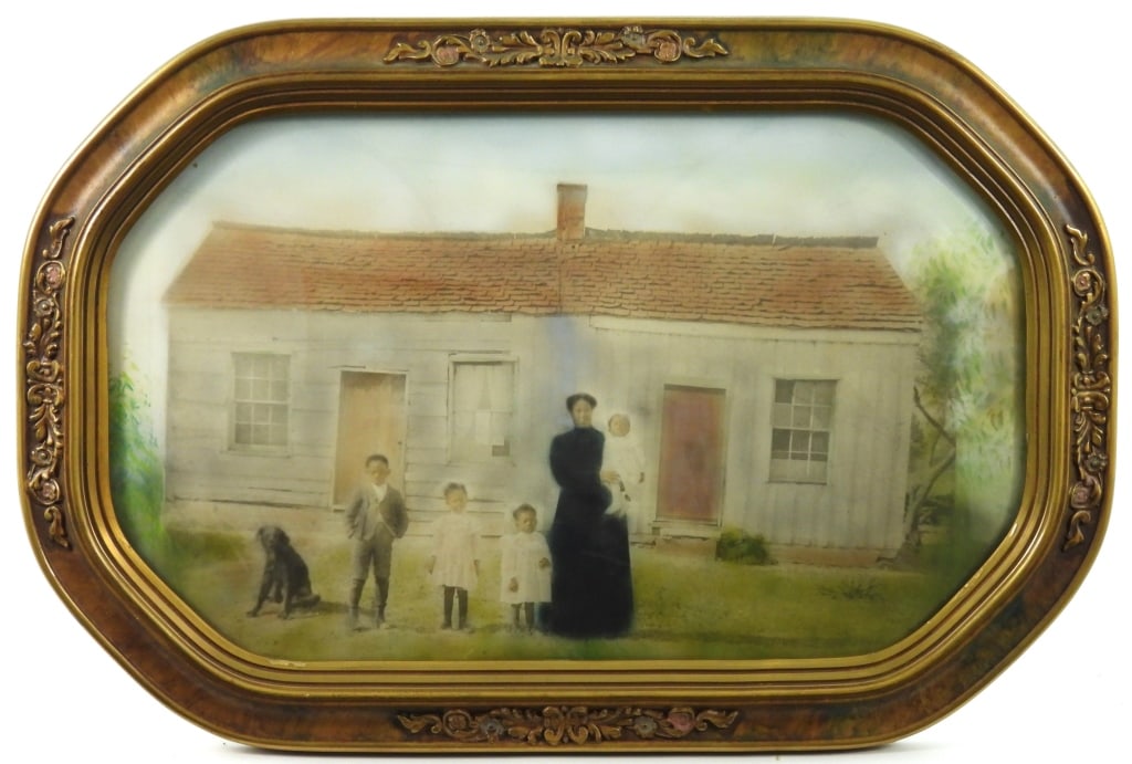 Framed Photograph Of African Americans & Dog: Hand tinted 2oth century photograph view of an Afro American family standing in front of a shared two family house. Antique convex glass frame measures 12" x 18" overall.