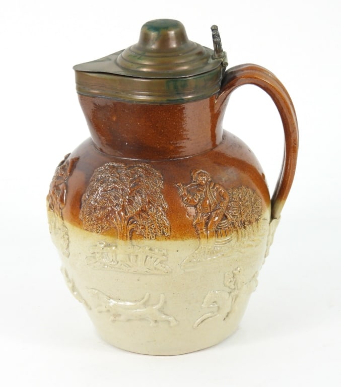 English Pottery Lidded Harvest Jug: Decorated with Dogs chasing a Deer, a Tavern scene, trees, and Hunt Horse with rider. Copper lid was silver washed, but that has worn off the outside surface. No makers marks observed. Measures 7"
