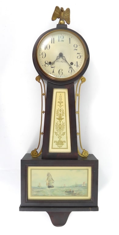 Nautical Scene New Haven Banjo Clock: Full sail ship with row boat in a harbor scene lower panel door. Eagle finial with brass body side rails. Measures 9-1-2" wide x 29" long x 3-1/2" deep. No key.