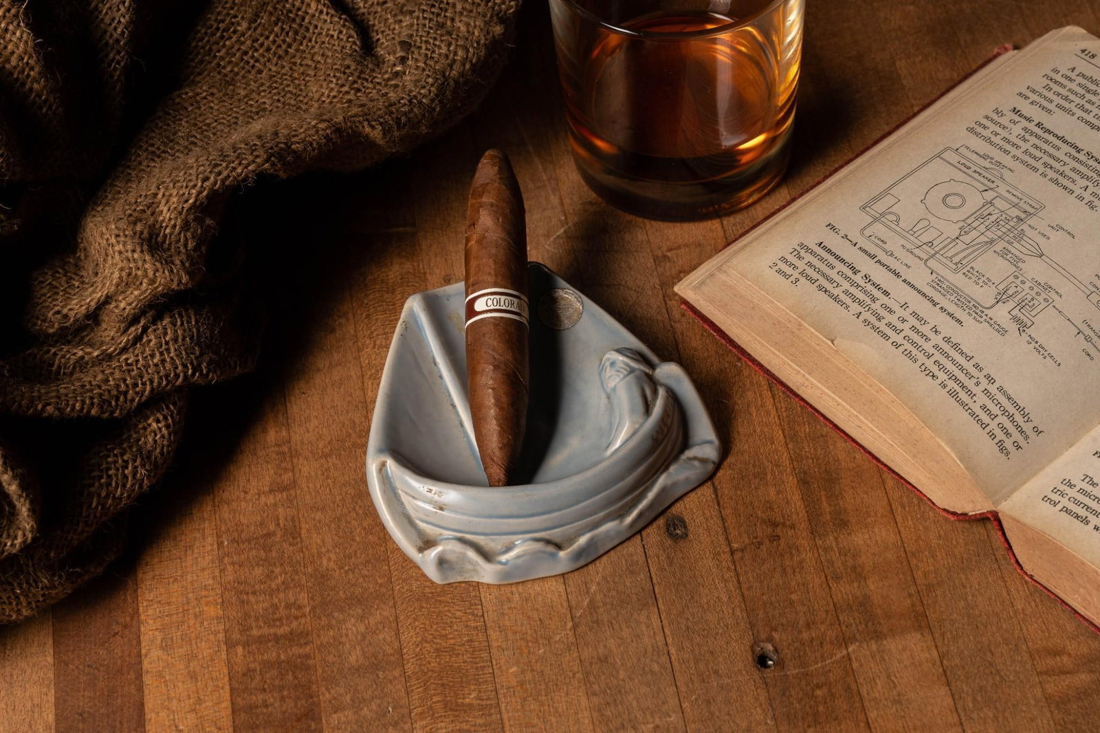 Blue Swedish Sailor Ashtray: Pale blue ceramic ashtray depicting an old sailor in a sailboat with "Sverige" (Sweden) marked on the side and maker's mark on the bottom. Also present is a tarnished inlaid coin. Exhibits