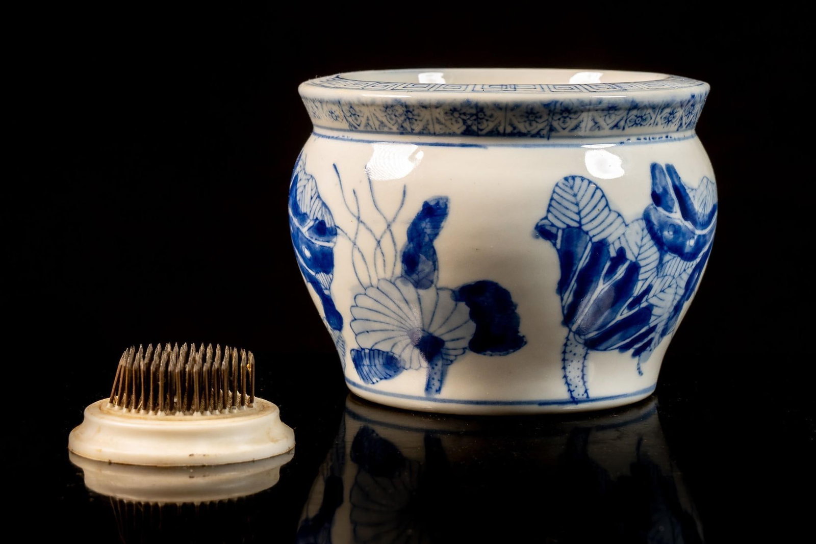 Vintage Chinese Qinghua Planter: Blue and white porcelain planter with a lotus and other aquatic flora motif across the surface with a meandros pattern along the top edge. Exhibits water stains/rust on bottom of interior. 6" dia 